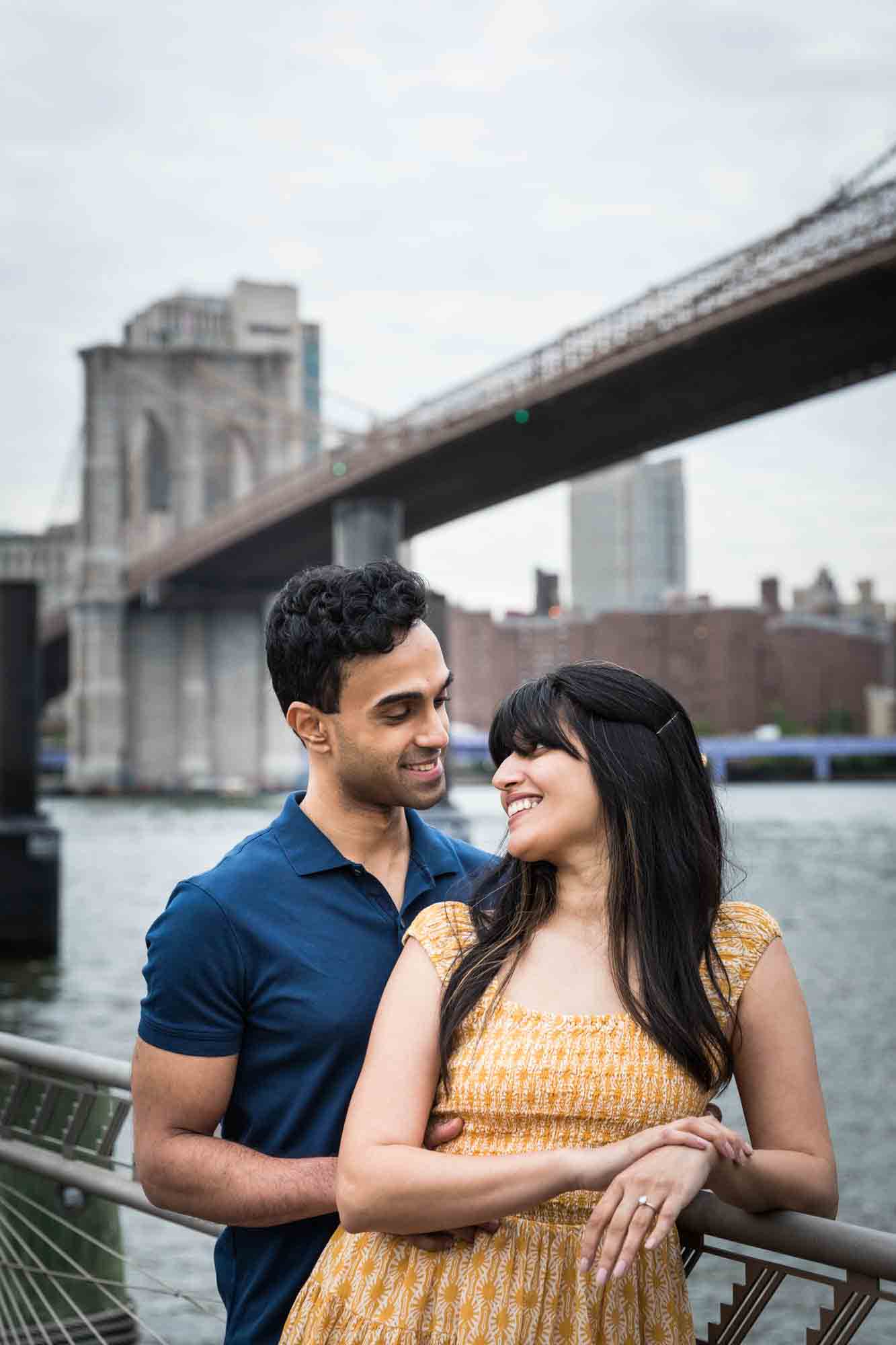 Woman in yellow dress and man in blue shirt standing together in front of Brooklyn Bridge