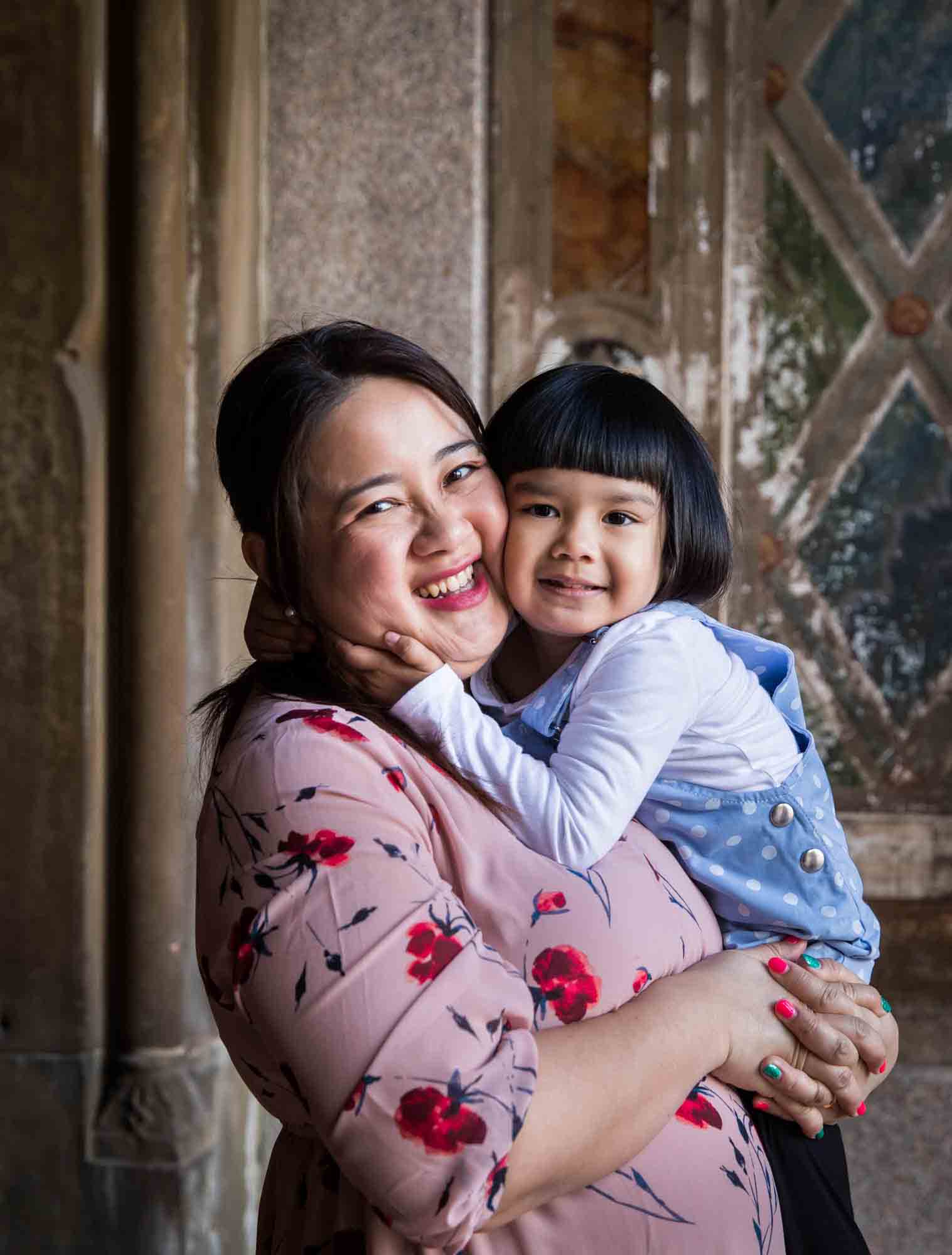 Little girl hugging her mother under Bethesda Terrace during a Central Park family portrait