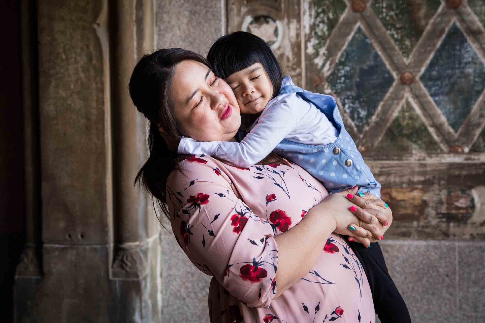 Little girl hugging her mother under Bethesda Terrace during a Central Park family portrait