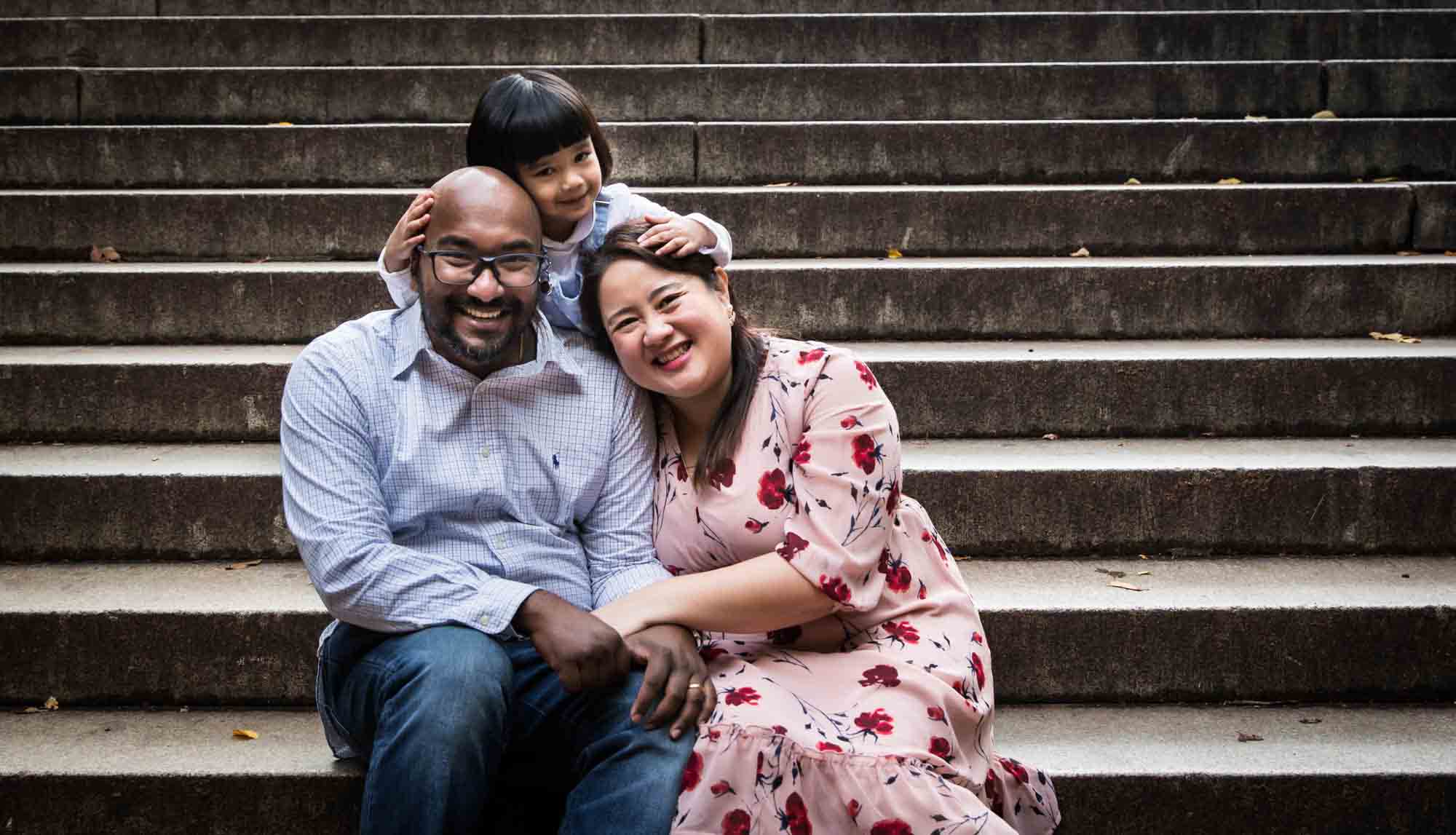 Little girl hugging both parents on steps of Bethesda Terrace for an article on Central Park winter portrait tips