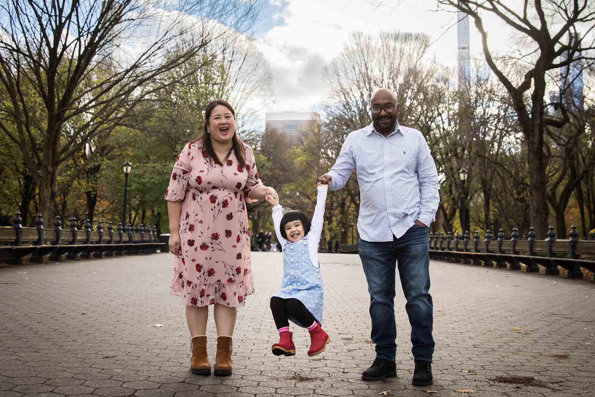 Parents swinging little girl between them in Central Park for an article on Central Park winter portrait tips