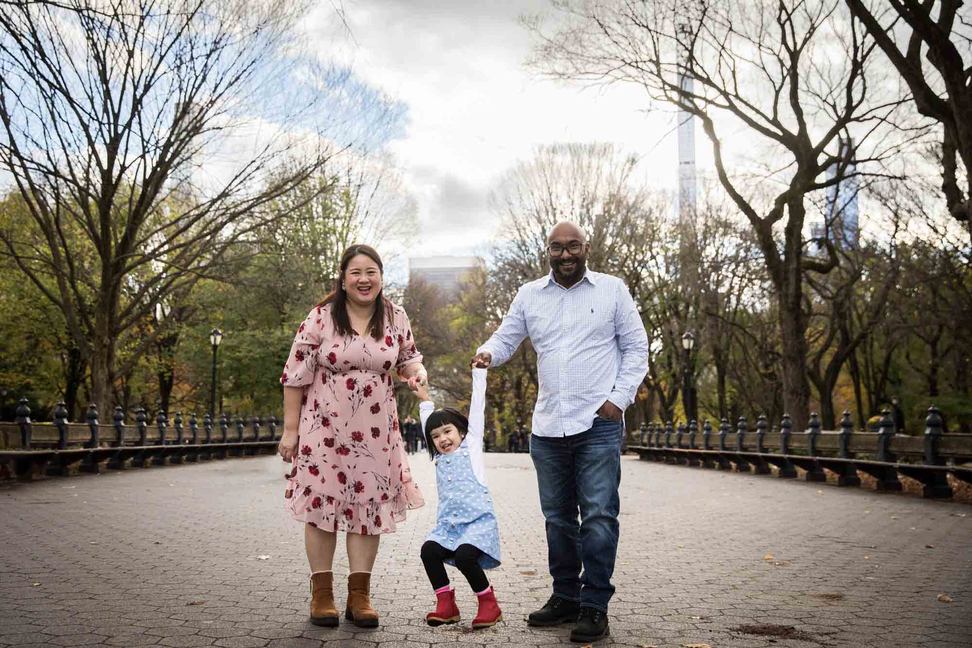 Parents swinging little girl between them in Central Park for an article on Central Park winter portrait tips