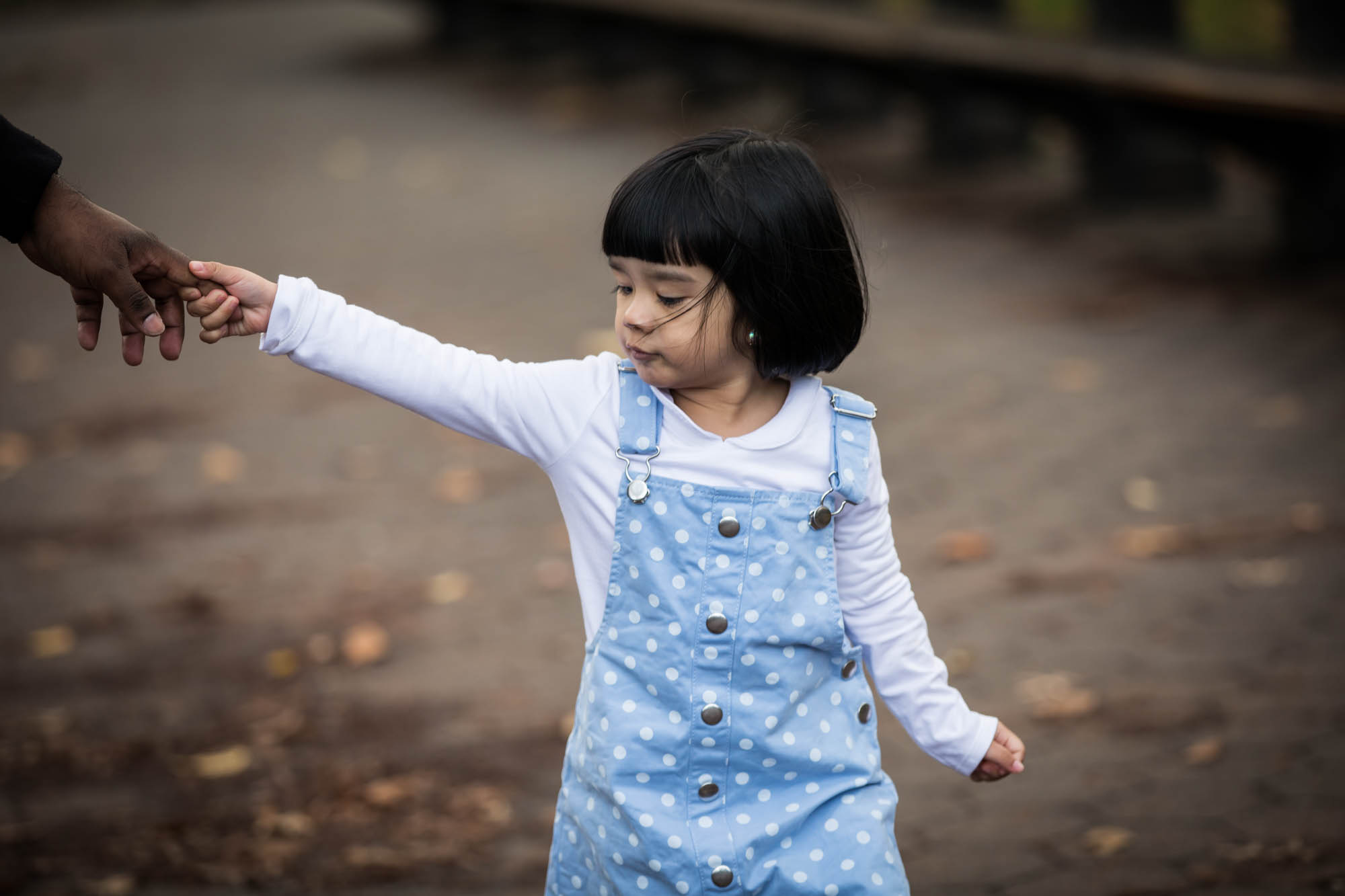 Little girl wearing blue dress and white shirt holding finger of parent for an article on Central Park winter portrait tips