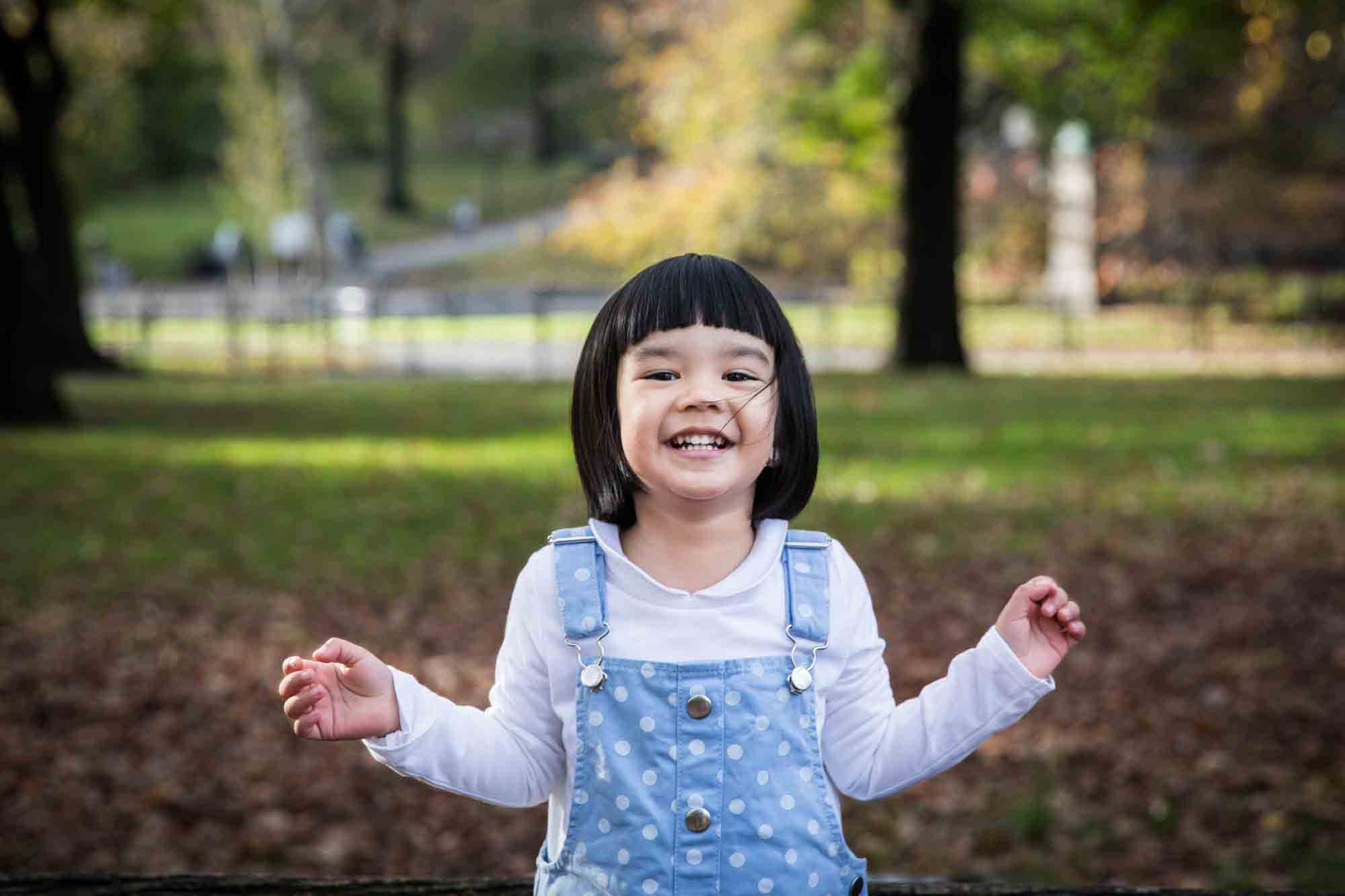 Smiling little girl wearing blue overalls and white shirt for an article on Central Park winter portrait tips