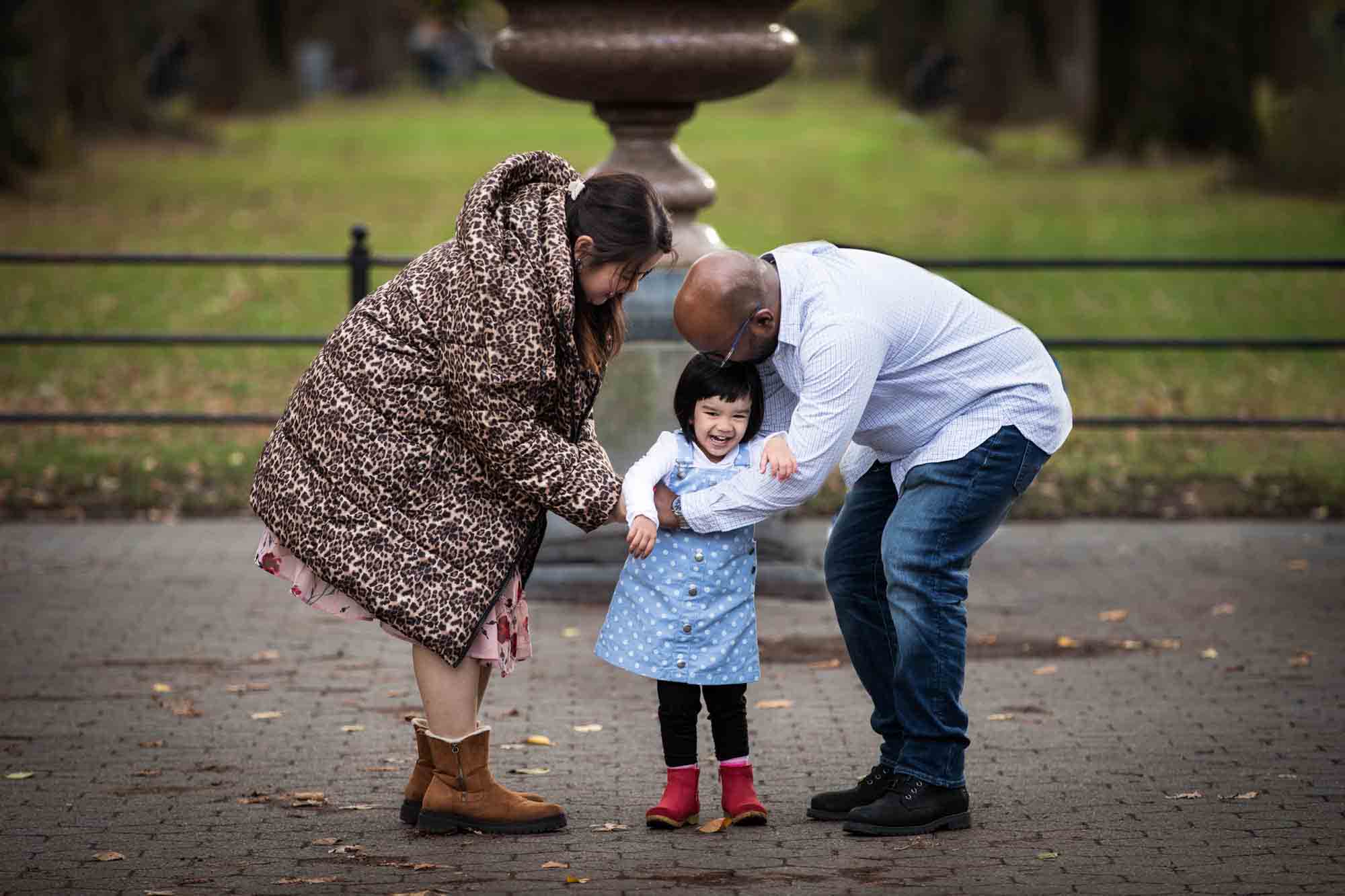 Parents playing with little girl wearing blue dress on the Mall during Central Park family portrait