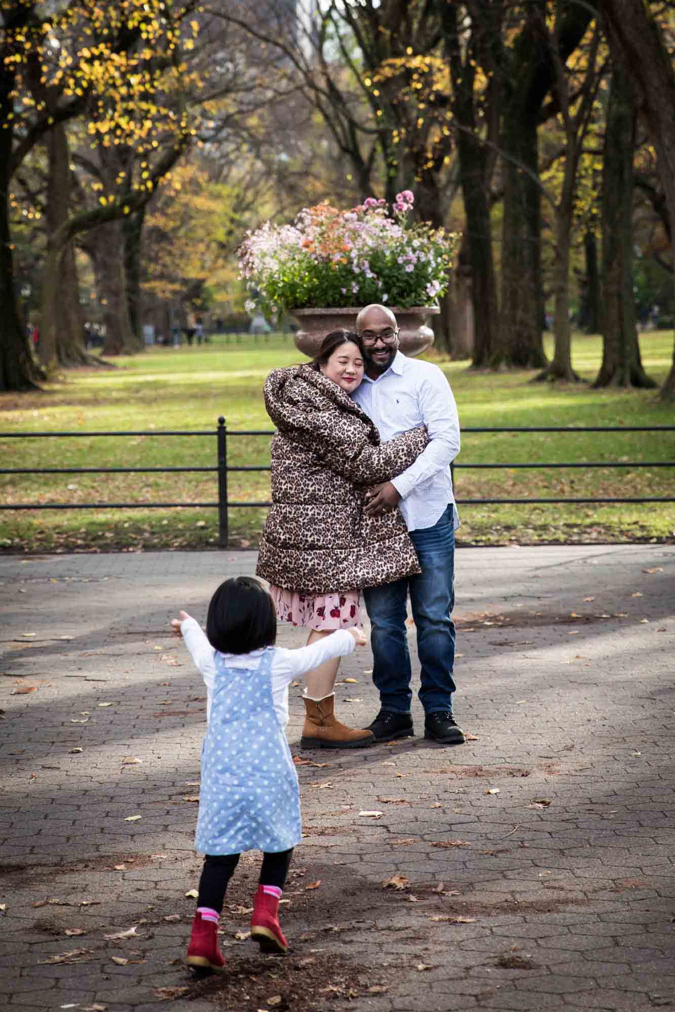 Parents playing with little girl wearing blue dress on the Mall during Central Park family portrait