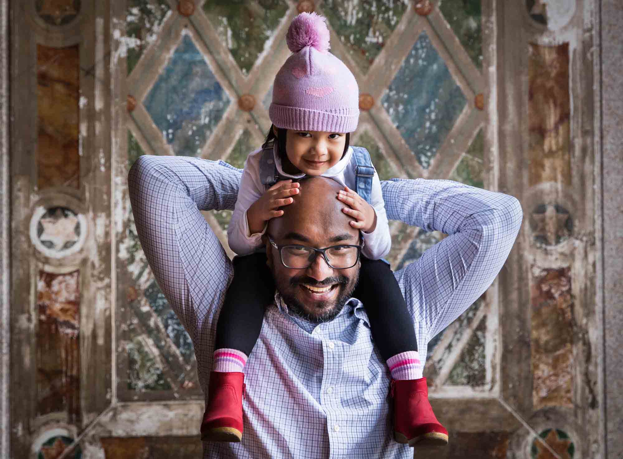 Little girl wearing knit cap and sitting on father's shoulders during a Central Park family portrait