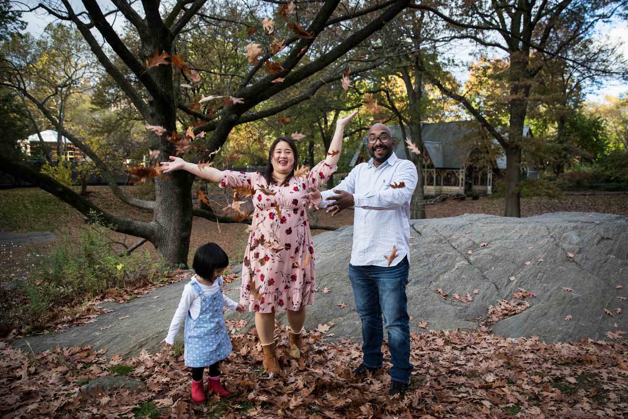 Central Park family portrait of parents playing in leaves with little girl 