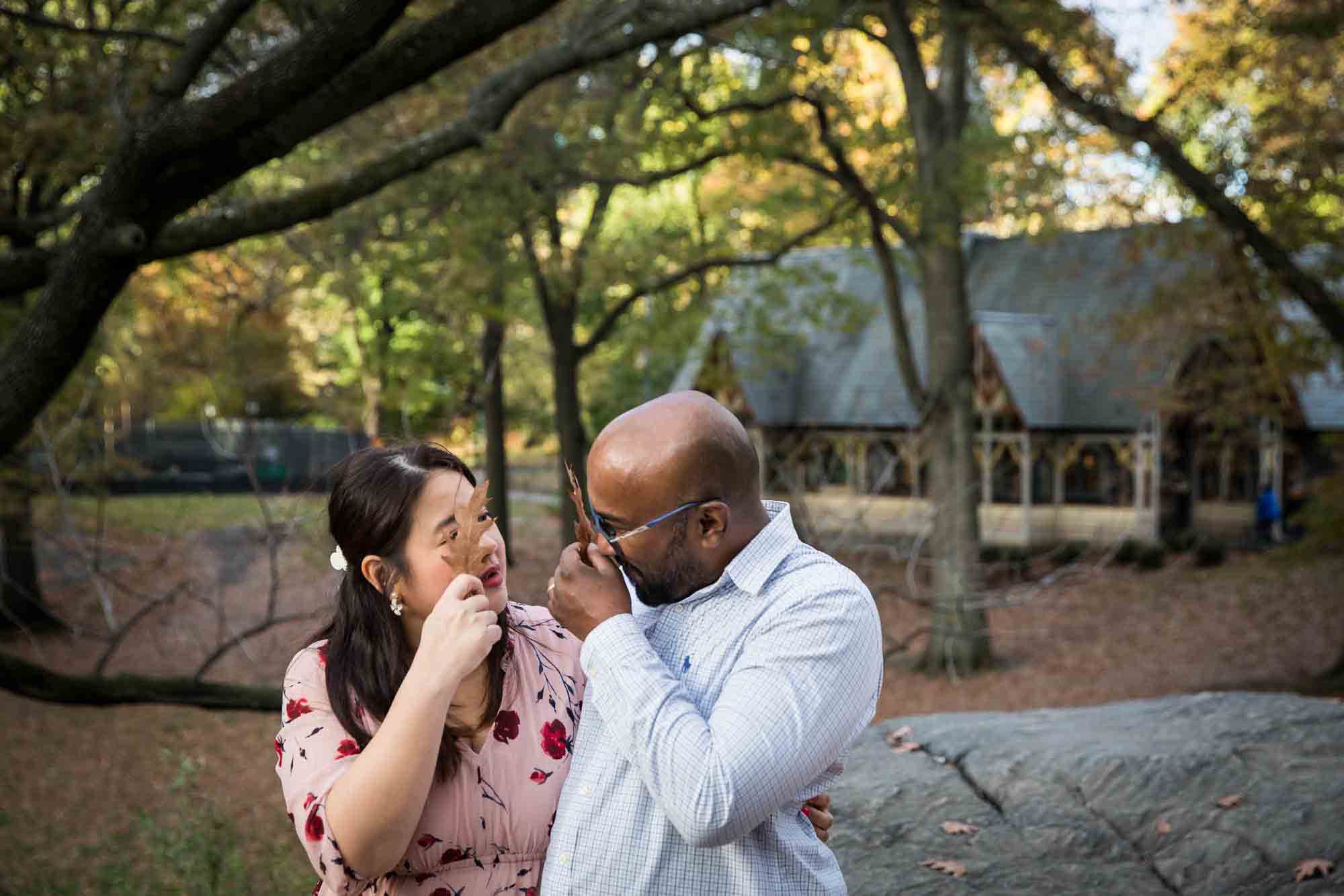 Central Park family portrait of couple playing peekaboo behind fall leaves
