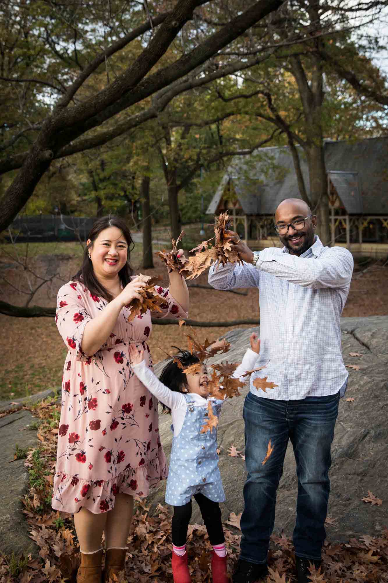 Central Park family portrait of parents playing in leaves with little girl 