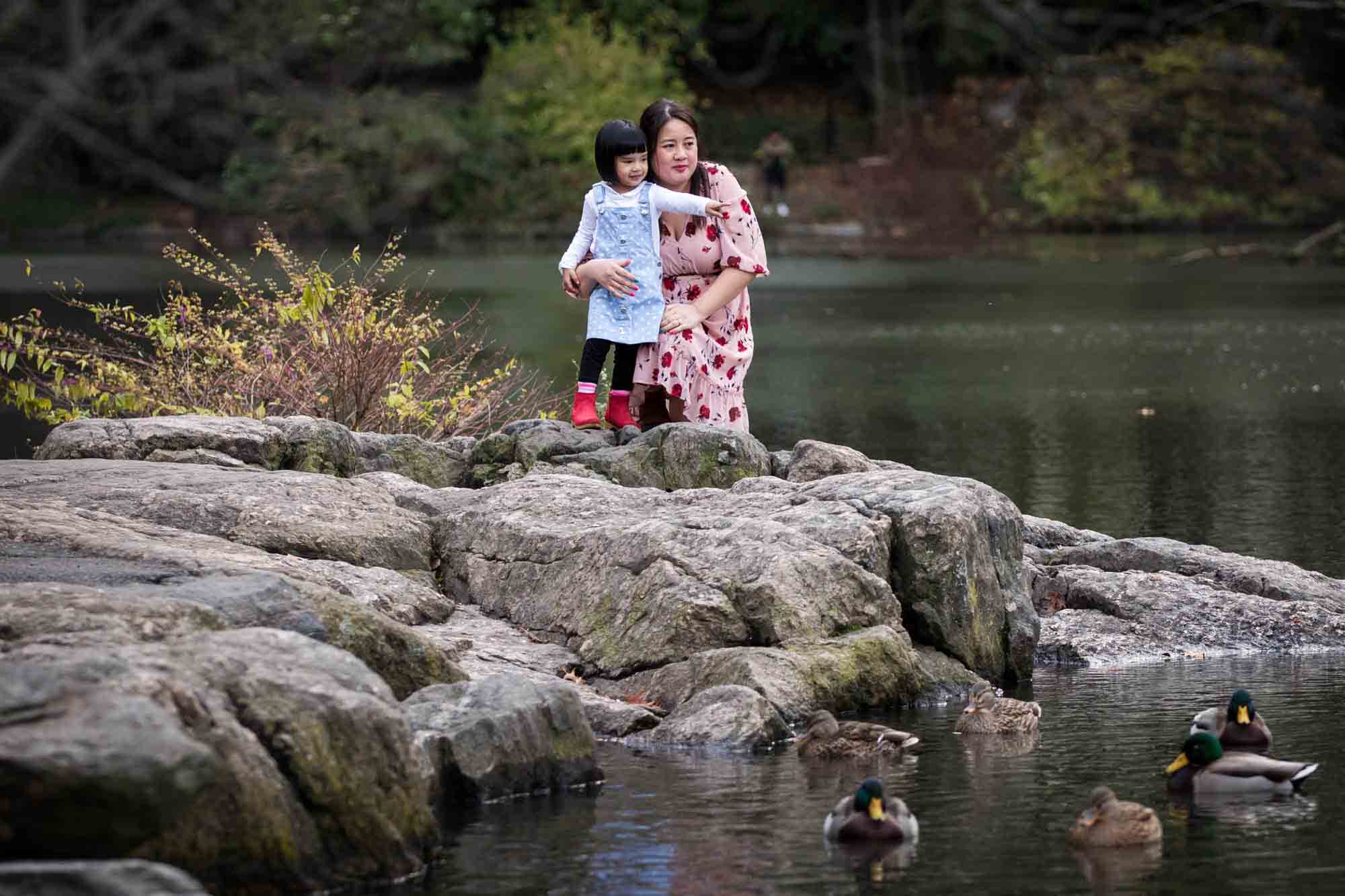 Mother pointing out ducks to little girl along lake for an article on Central Park winter portrait tips