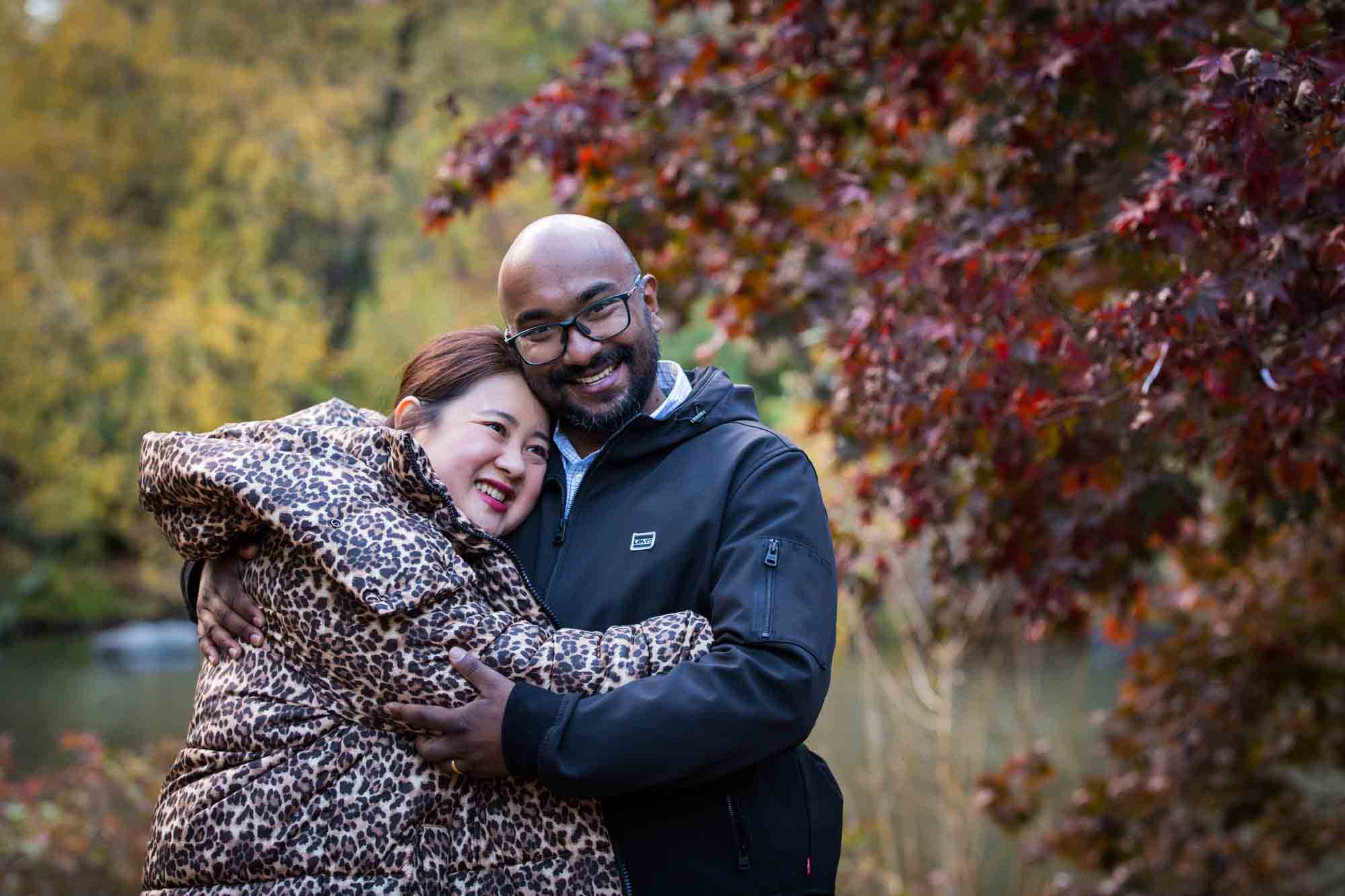 Couple hugging in front of tree with red leaves for an article on Central Park winter portrait tips
