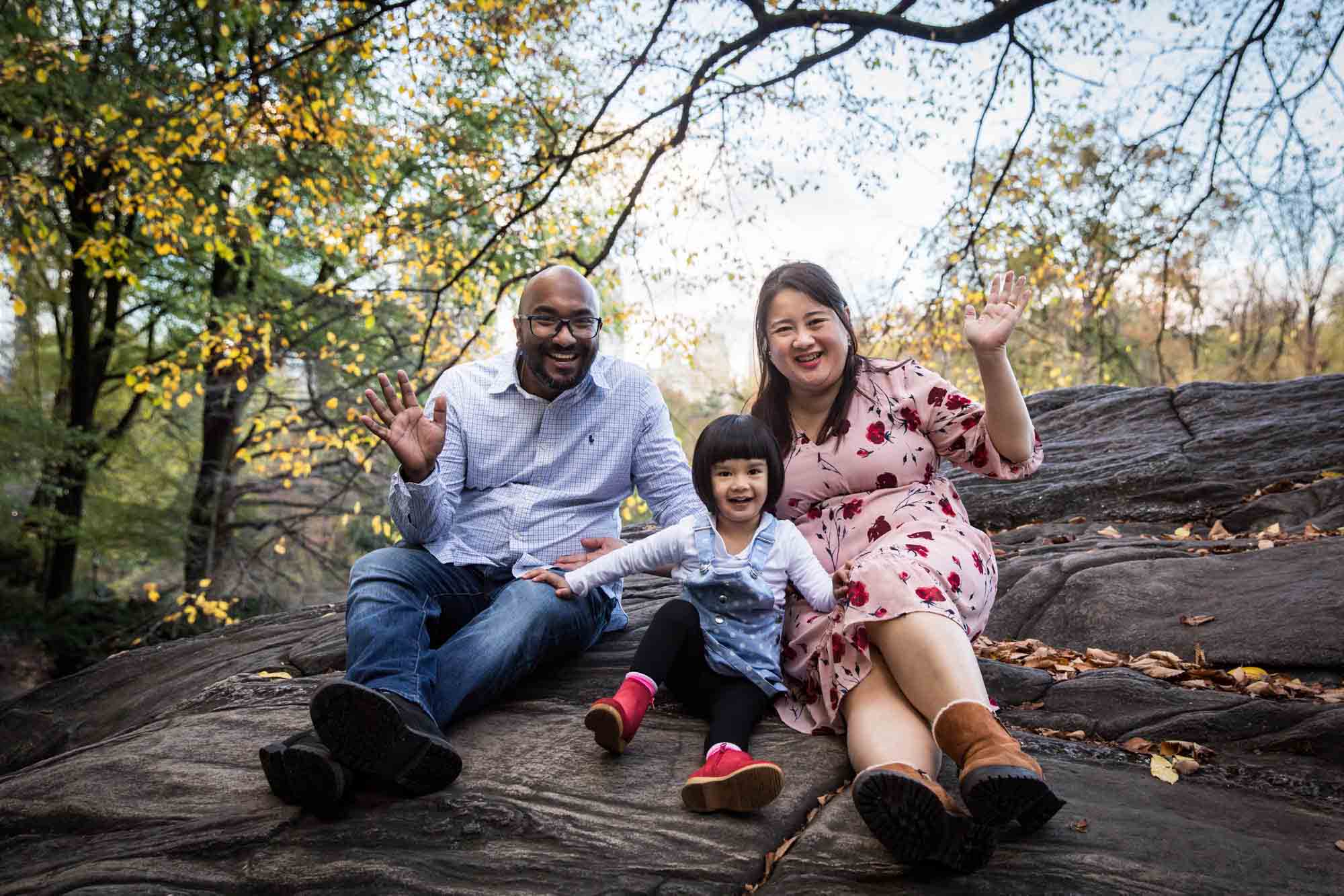 Parents and little girl sitting on large rock for an article on Central Park winter portrait tips