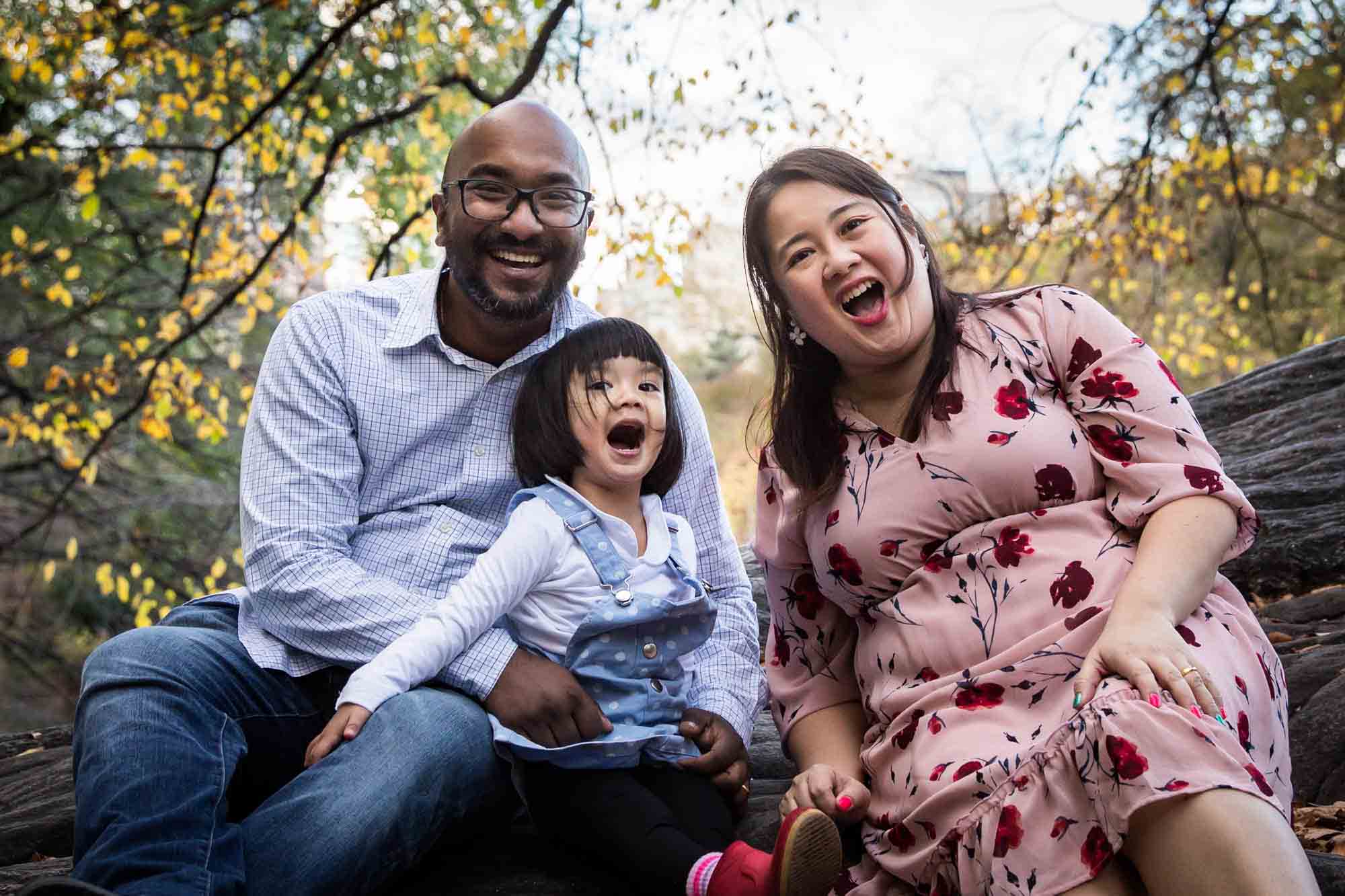 Parents and little girl sitting on large rock for an article on Central Park winter portrait tips