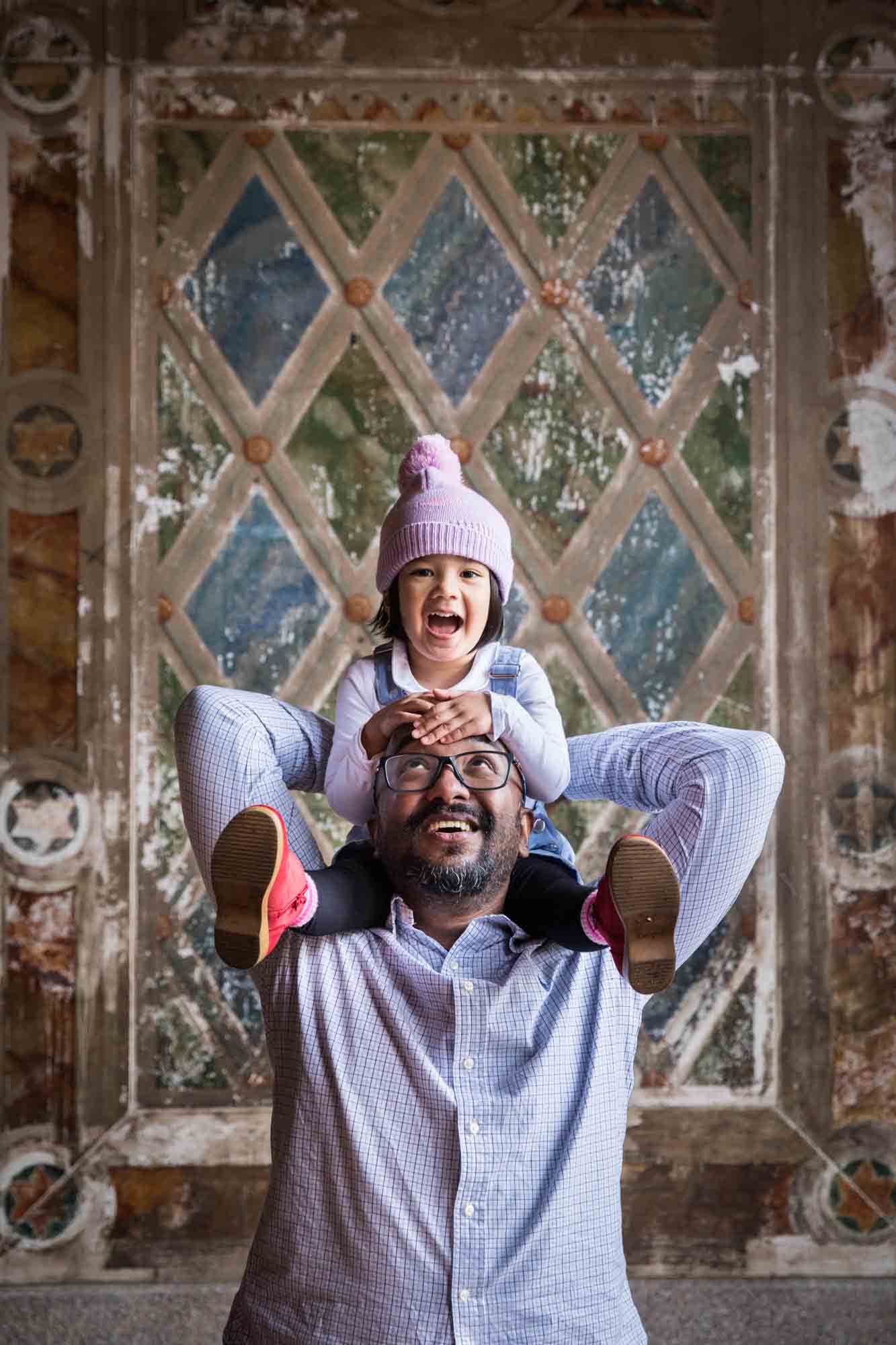 Little girl wearing knit cap and sitting on father's shoulders during a Central Park family portrait