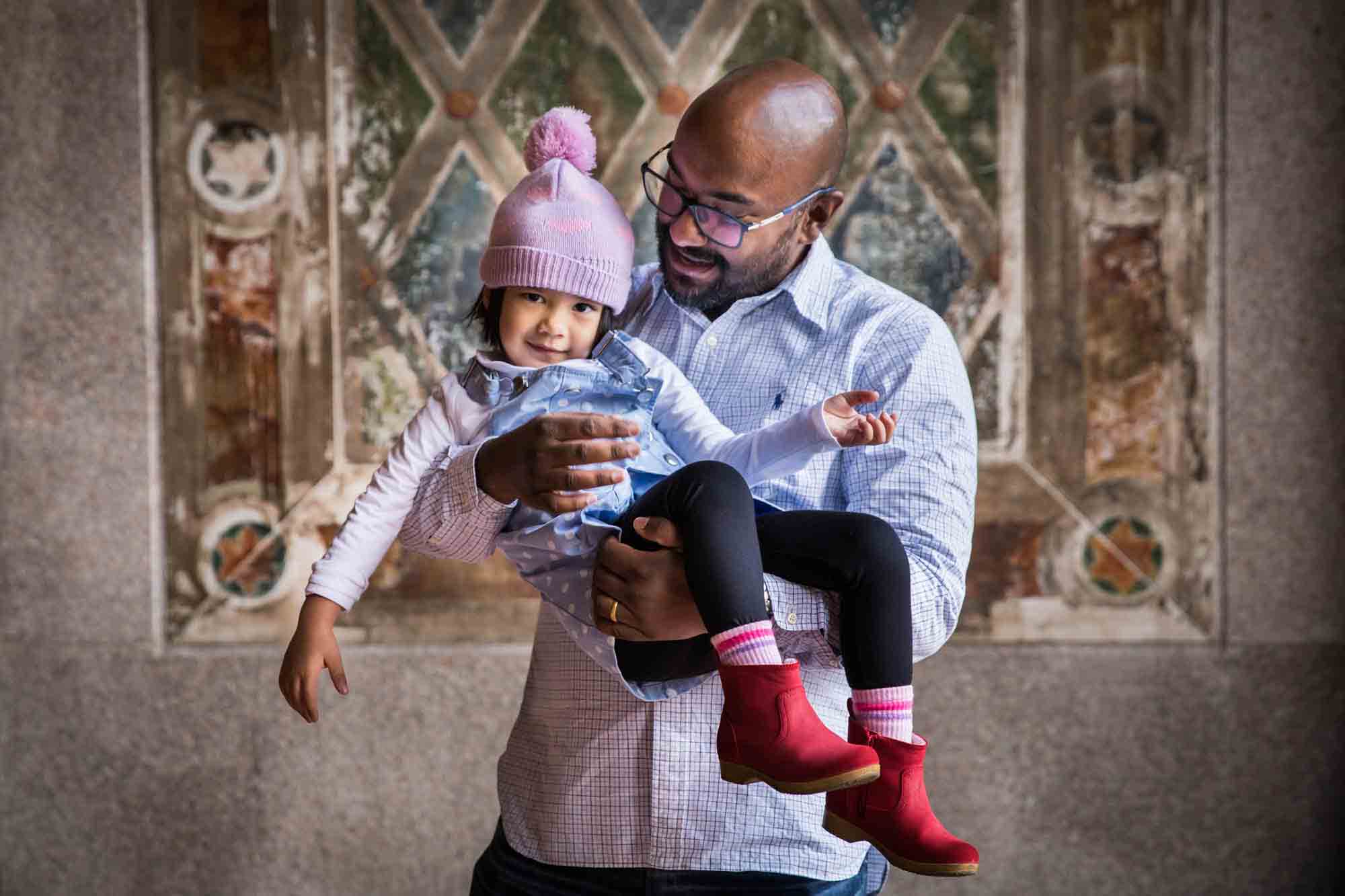 Father holding little girl wearing knit cap during a Central Park family portrait