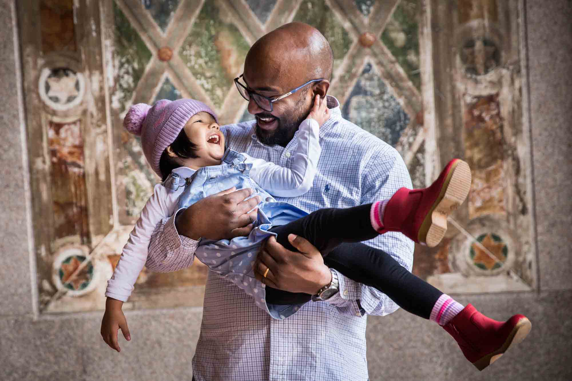 Father holding little girl wearing knit cap during a Central Park family portrait