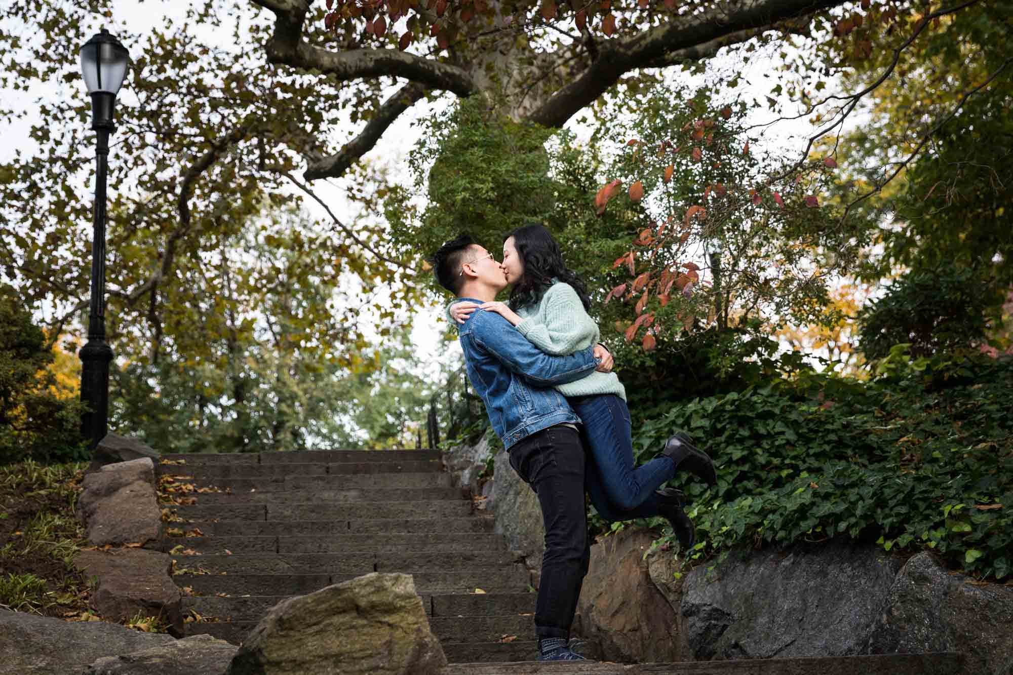 Fort Tryon Park engagement photo of man lifting woman up while kissing on stone stairway