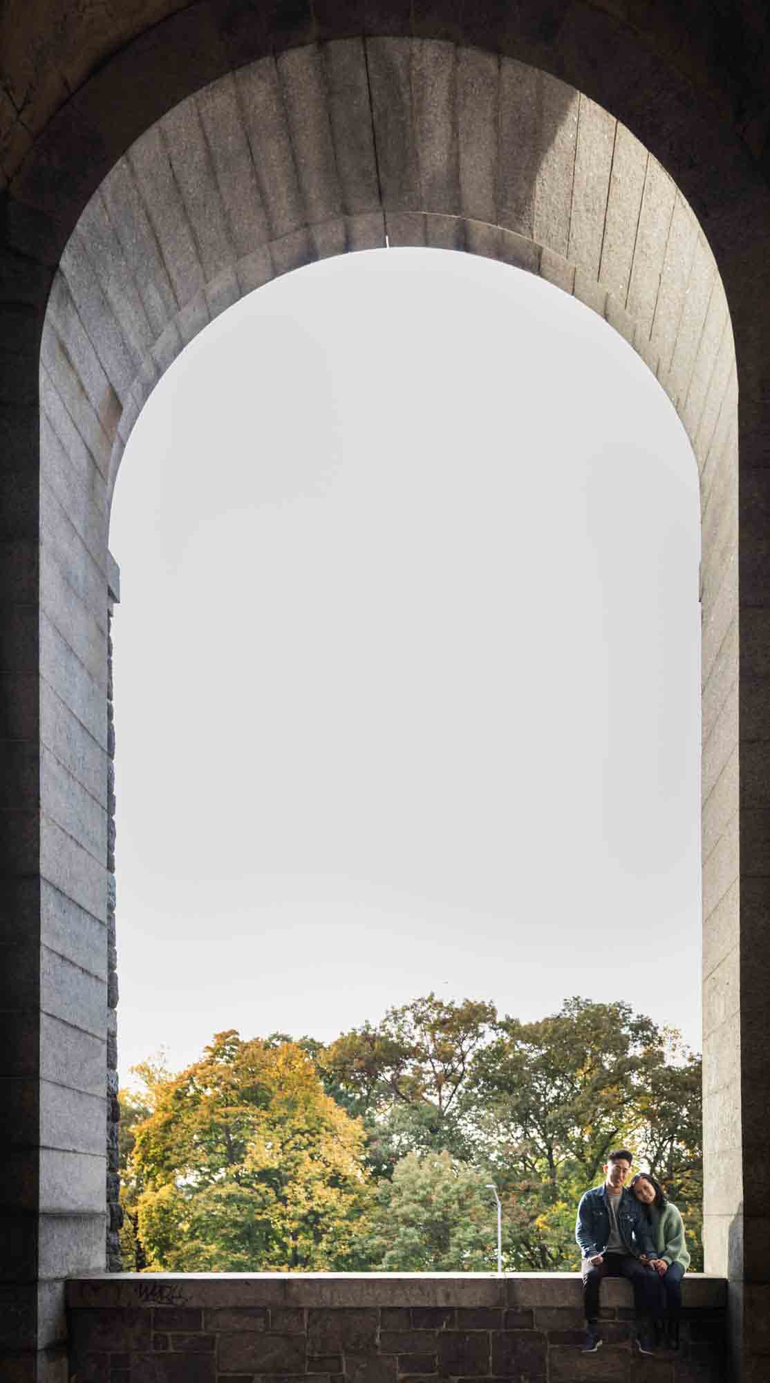 Couple sitting under arch in Billings Arcade at a Fort Tryon Park engagement photo shoot