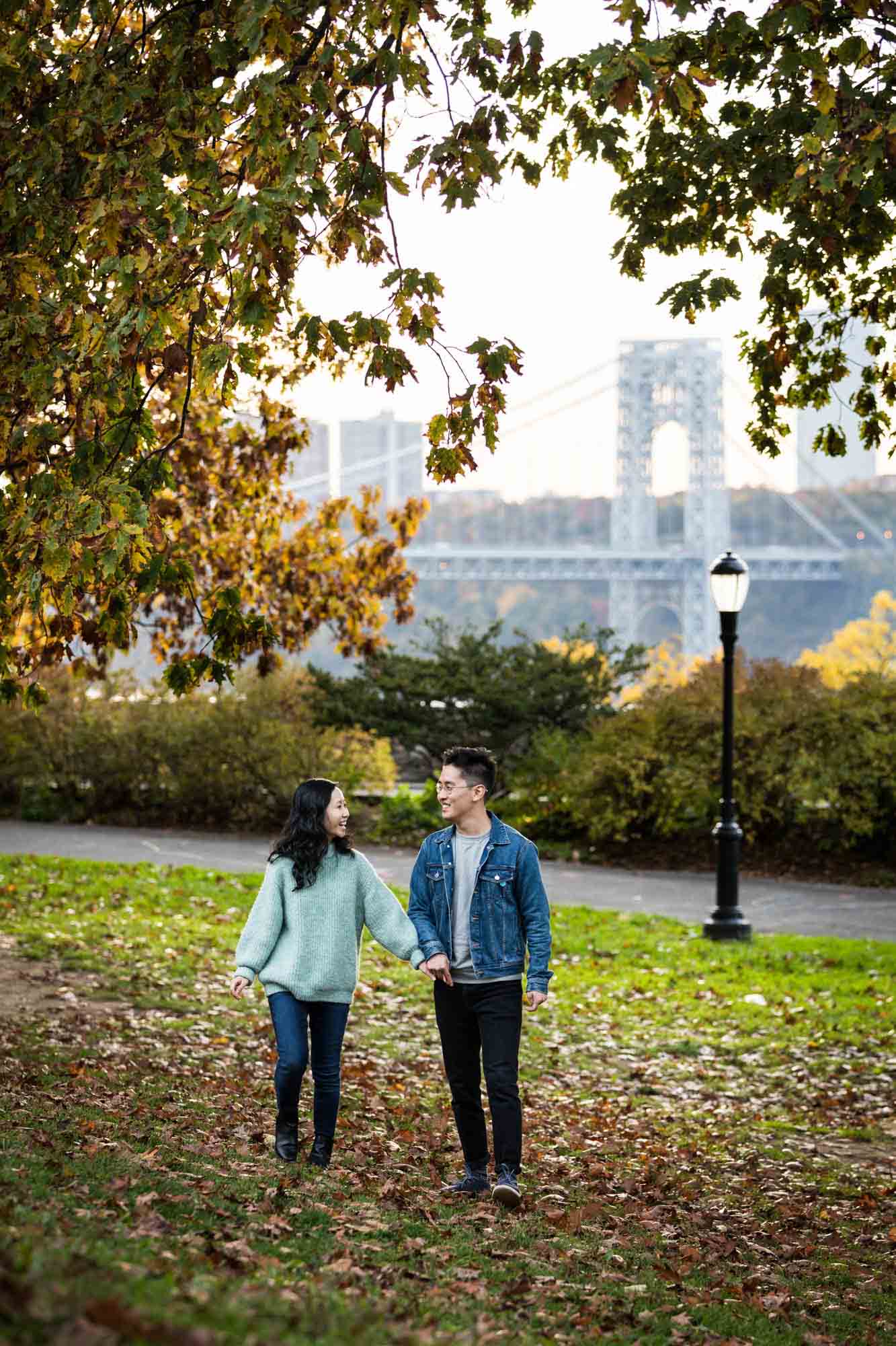 Couple walking hand in hand across grassy field at a Fort Tryon Park engagement photo shoot