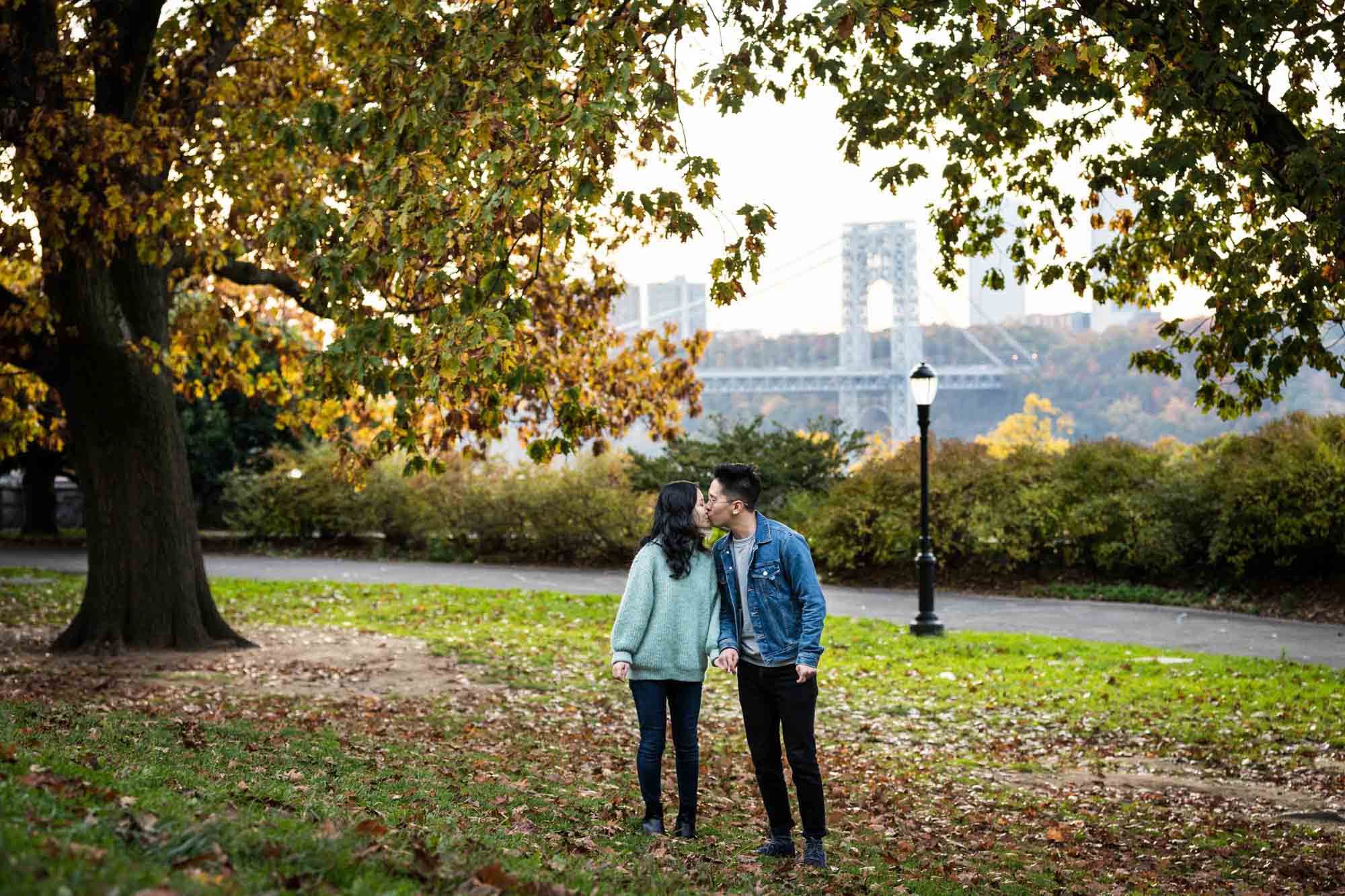Fort Tryon Park engagement photos of couple holding hands and kissing in middle of field