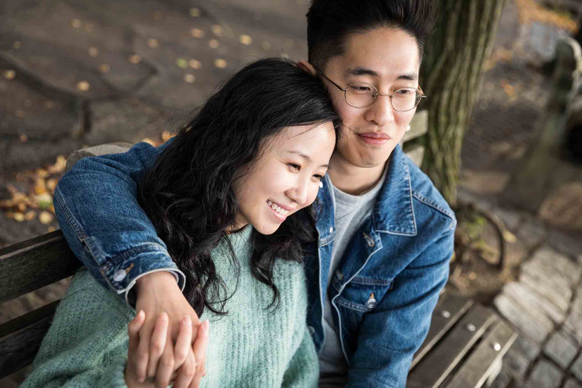 Fort Tryon Park engagement photos of couple cuddled together on park bench with arms around each other