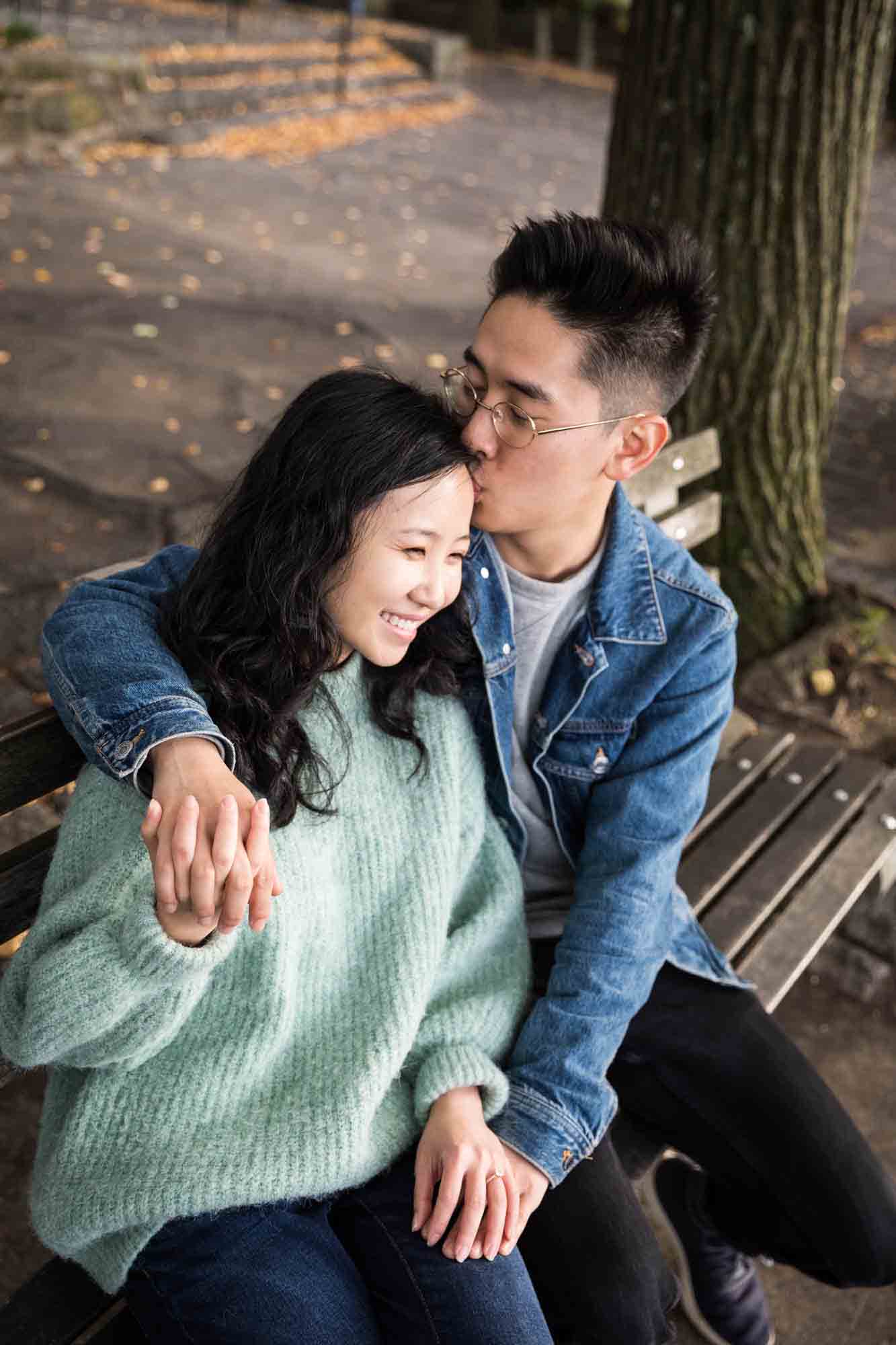 Fort Tryon Park engagement photo of man kissing woman on the side of the head on a bench