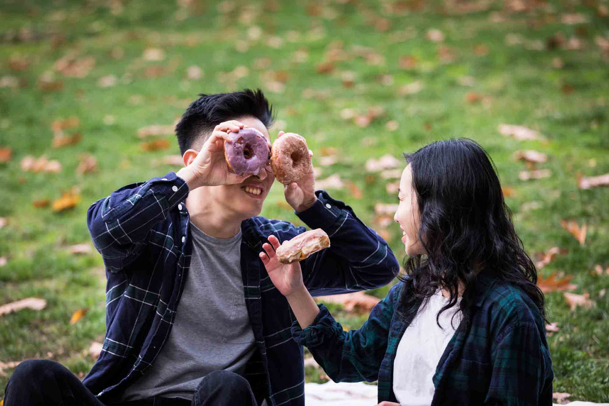 Fort Tryon Park engagement photo of man looking at woman through two colorful doughnuts