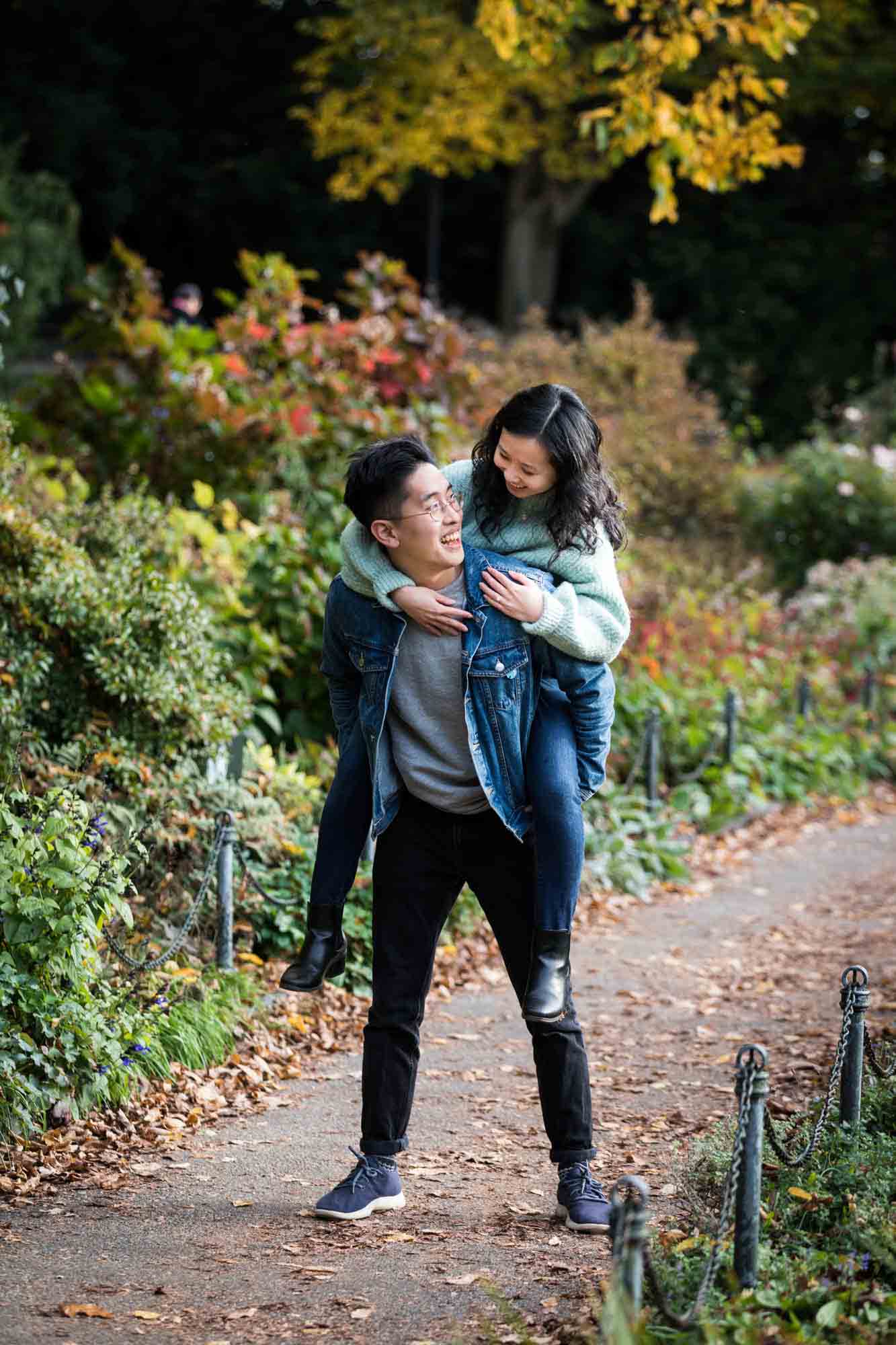 Fort Tryon Park engagement photo of man giving woman a piggyback ride in Heather Garden