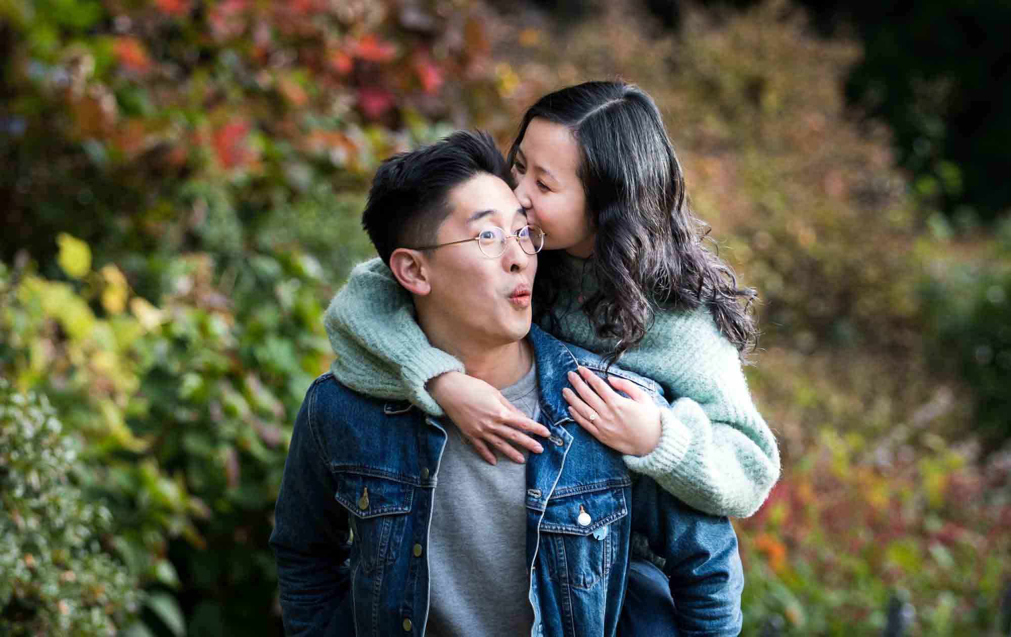 Fort Tryon Park engagement photos of woman kissing man on side of head in Heather Garden
