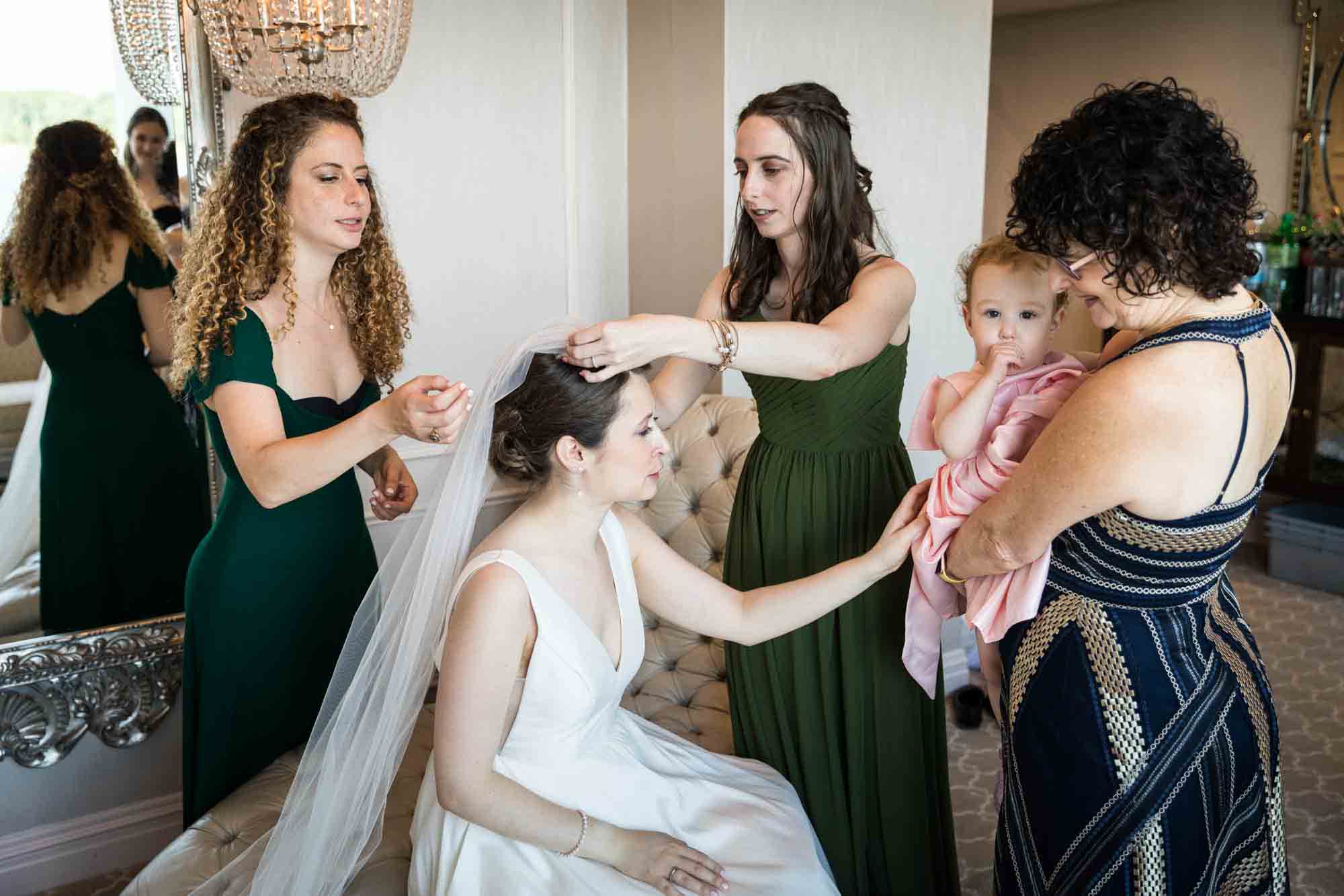 Glen Island Harbour Club wedding photos of bridesmaids adjust bride's veil as bride pets baby