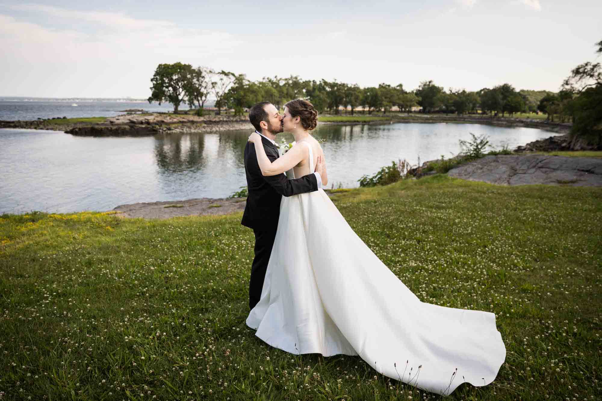 Glen Island Harbour Club wedding photos of bride and groom kissing in grass in front of Long Island Sound