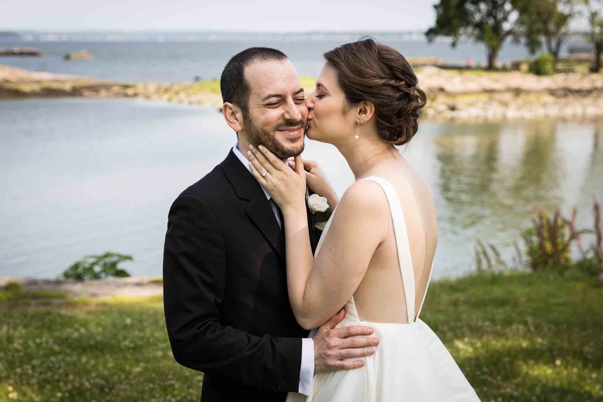 Glen Island Harbour Club wedding photos of bride kissing groom on the cheek in front of Long Island Sound
