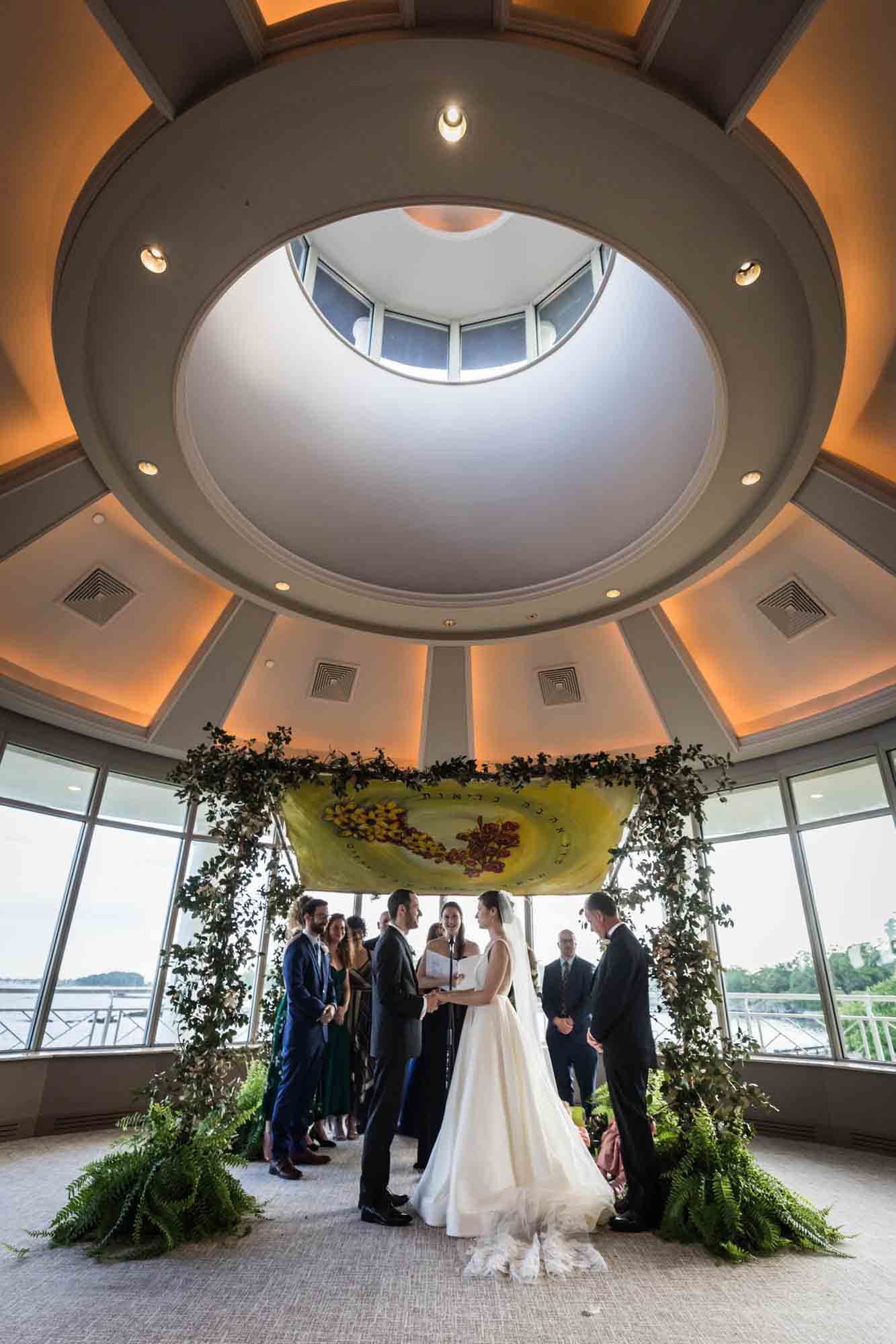 Bride, groom, and bridal party under chuppah at a at a Glen Island Harbour Club wedding ceremony