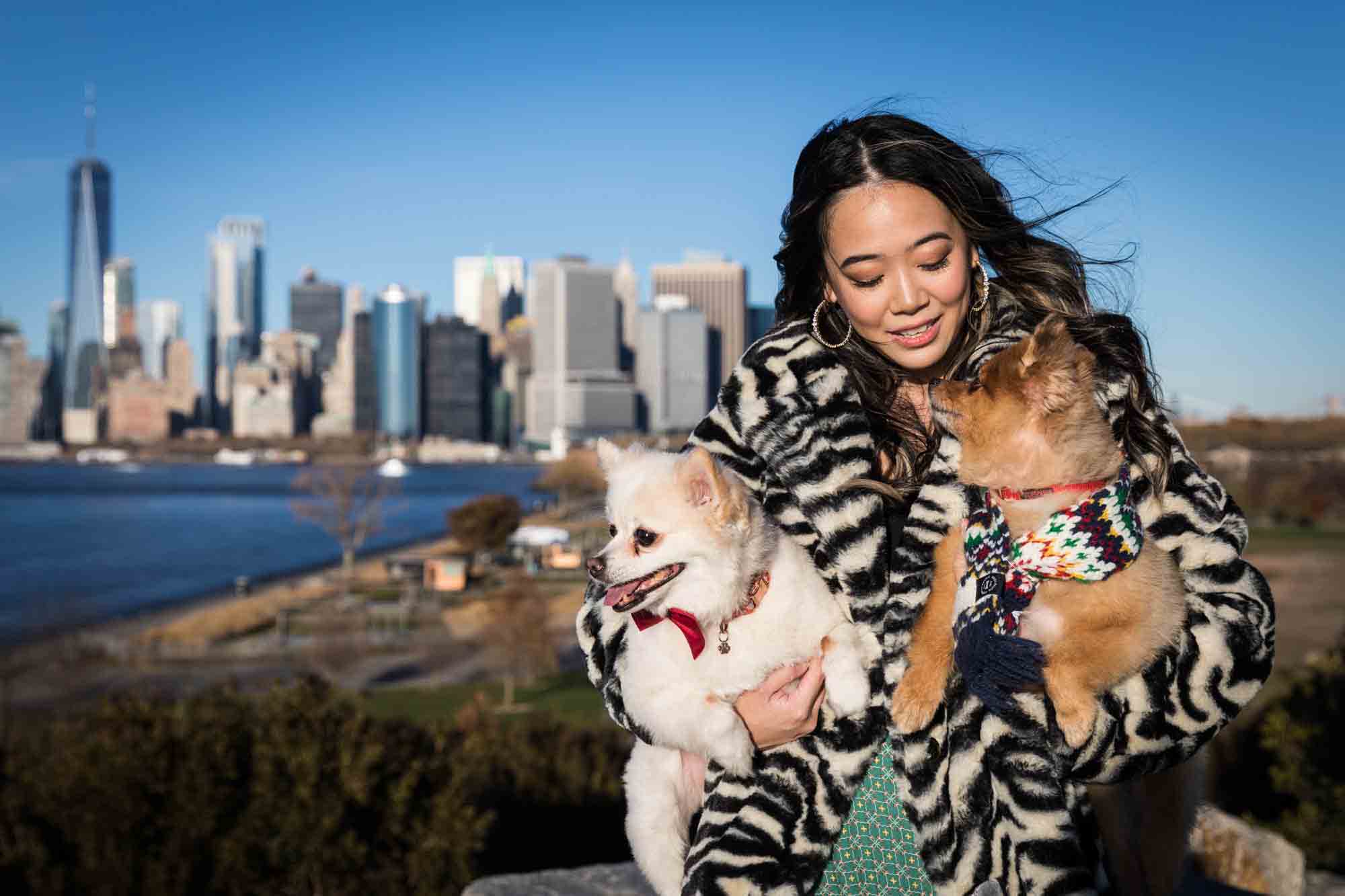 NYC pet portrait of woman holding two Pomeranian dogs with NYC skyline in background