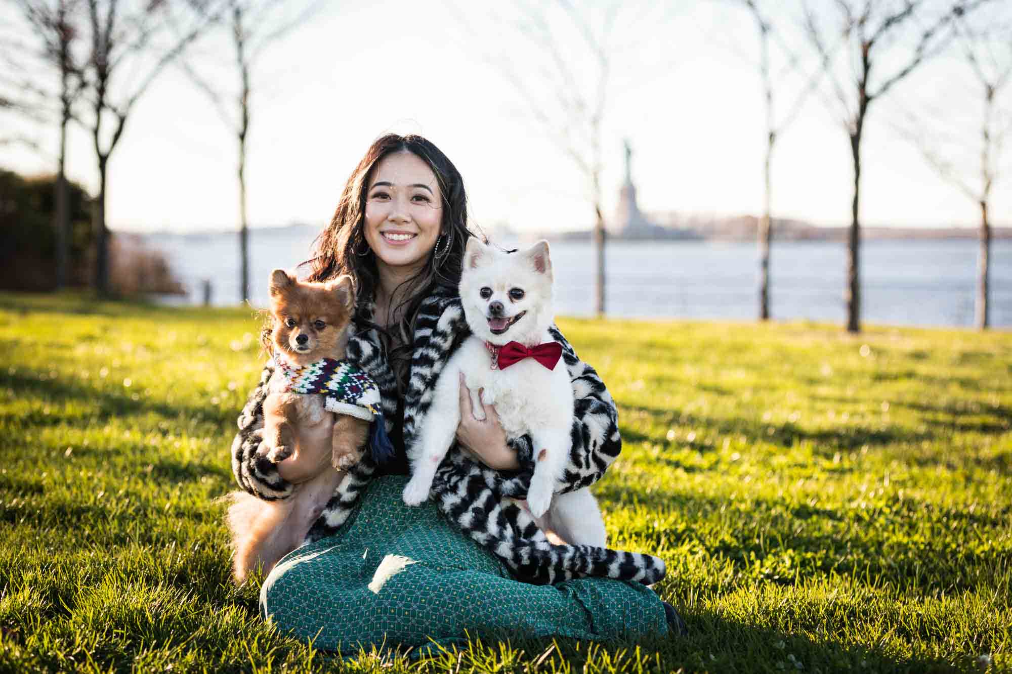 Pet portraits on Governors Island of woman sitting in grass holding two Pomeranian dogs