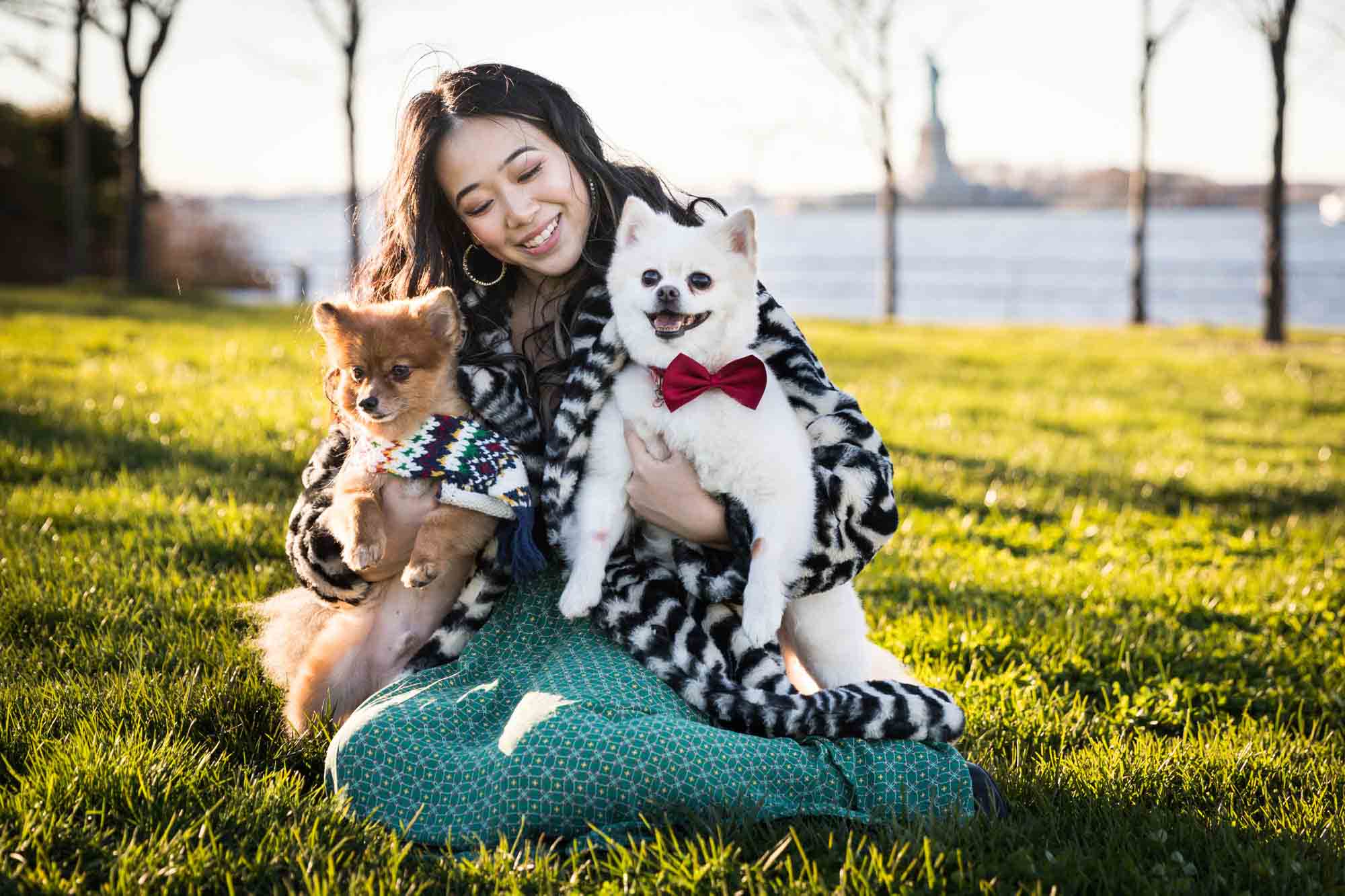 Pet portraits on Governors Island of woman sitting in grass holding two Pomeranian dogs