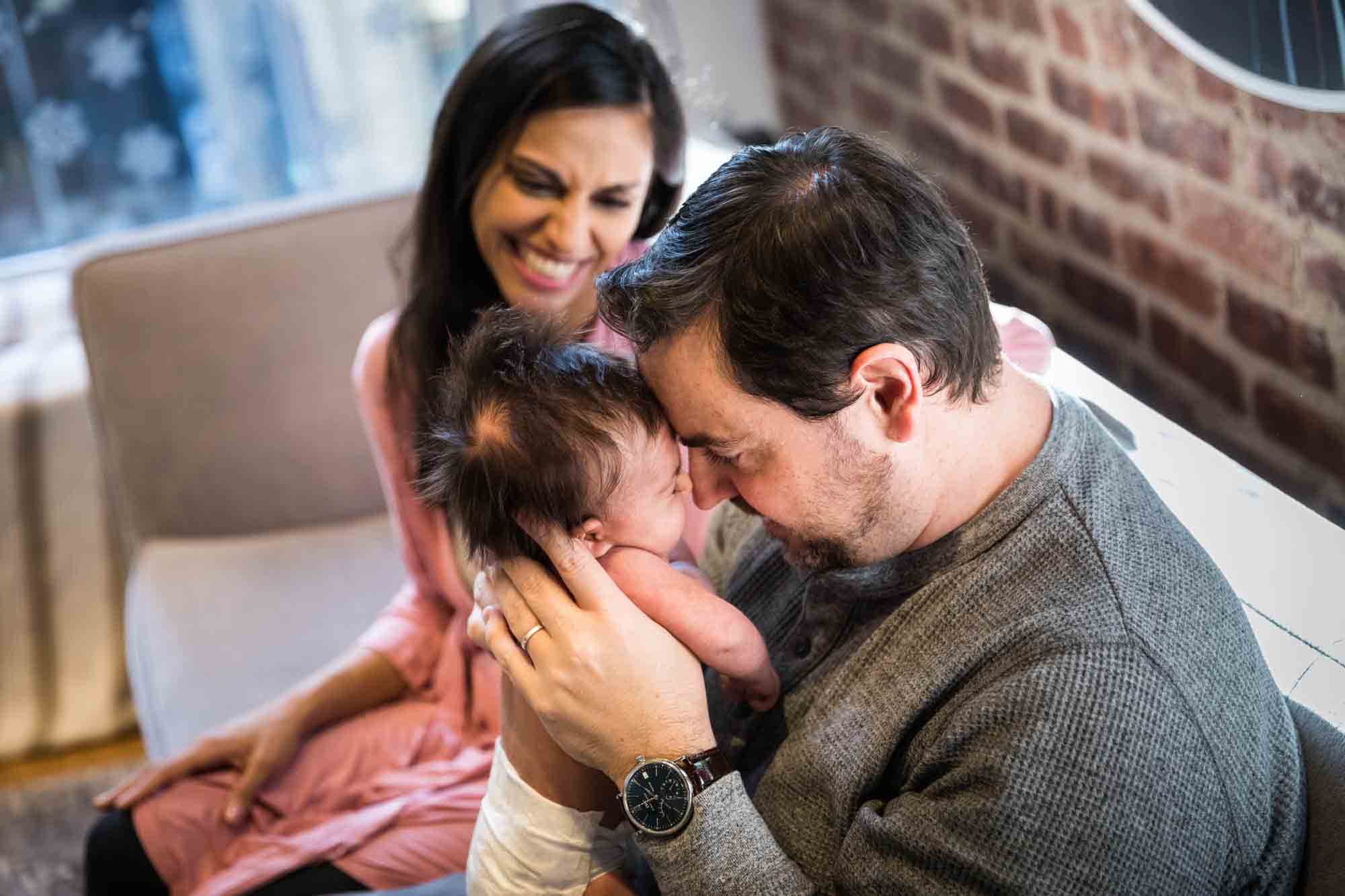 Mother watching as father touches his forehead to newborn baby