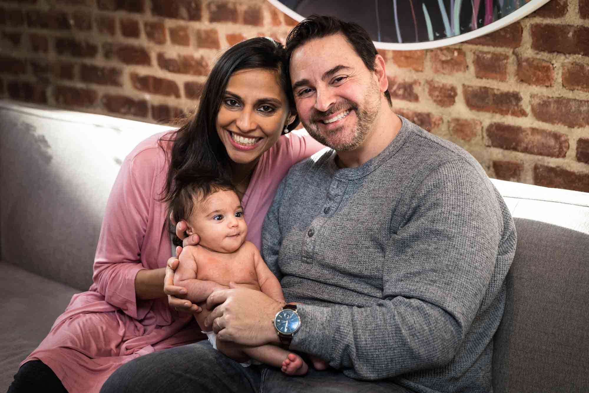 Parents smiling with newborn baby in front of brick wall