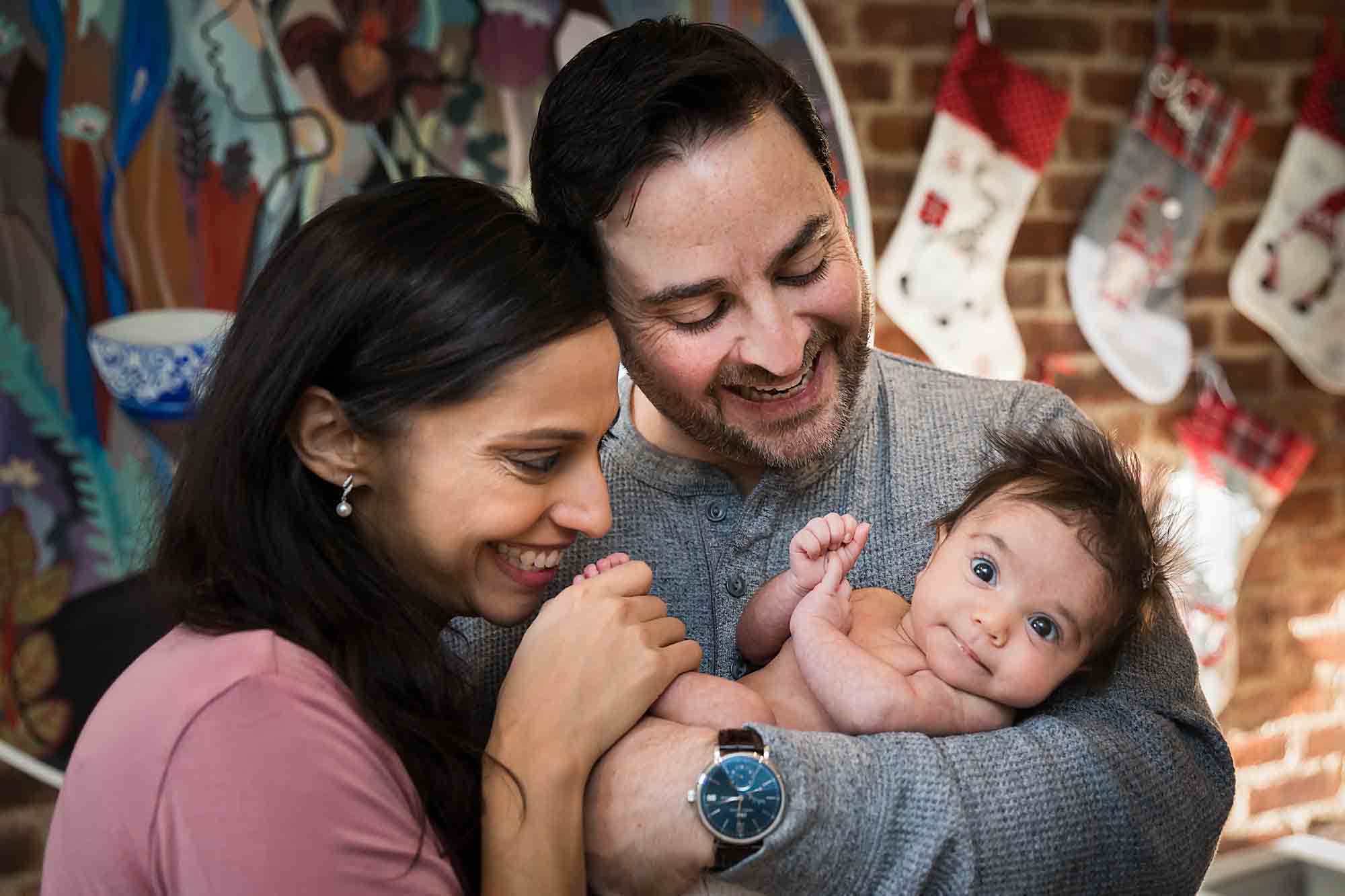 Parents holding newborn baby in front of brick wall