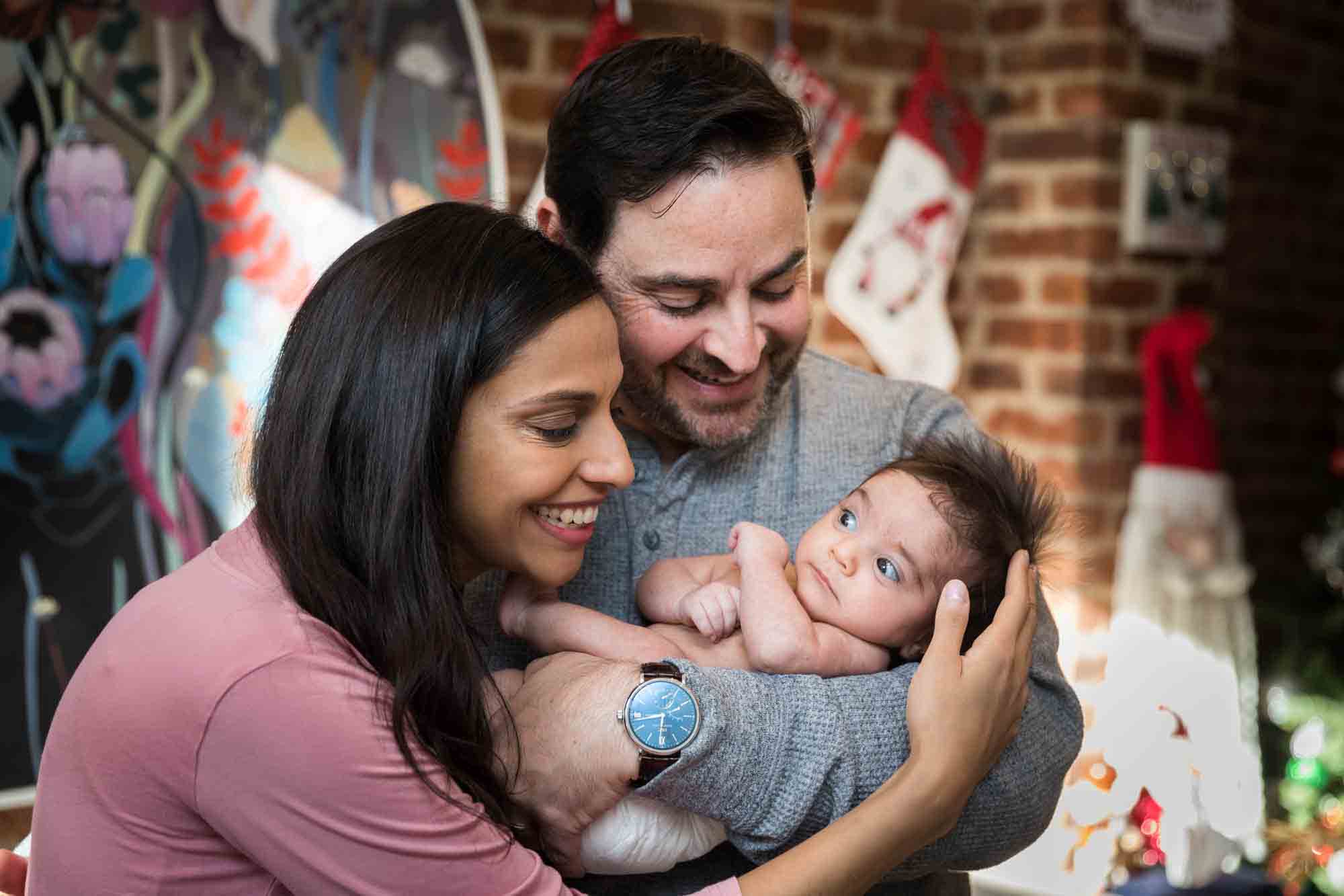 Parents holding newborn baby in front of brick wall