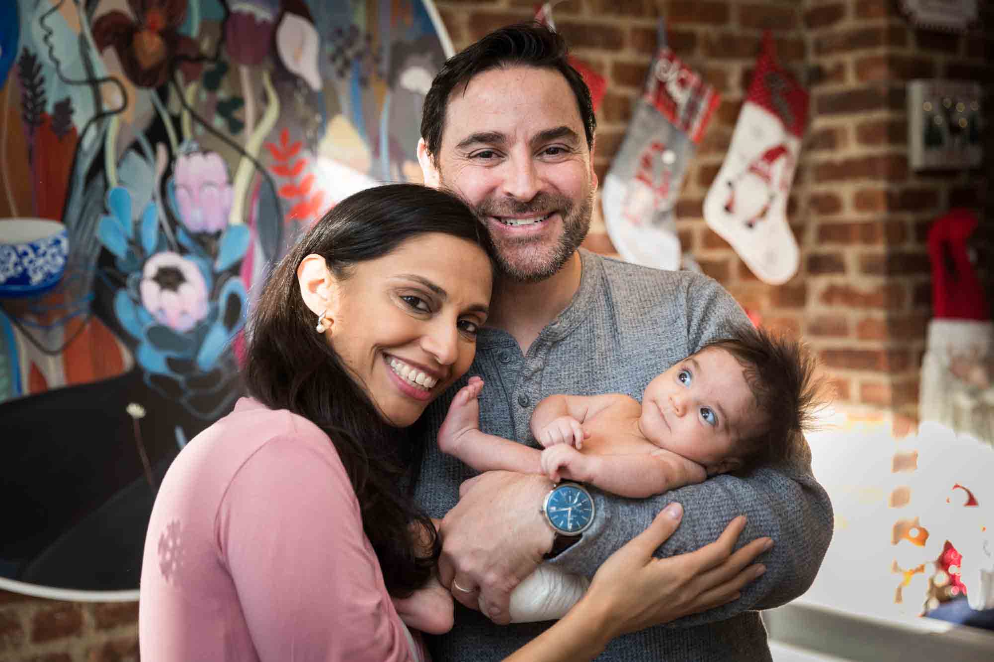 Parents holding newborn baby in front of brick wall