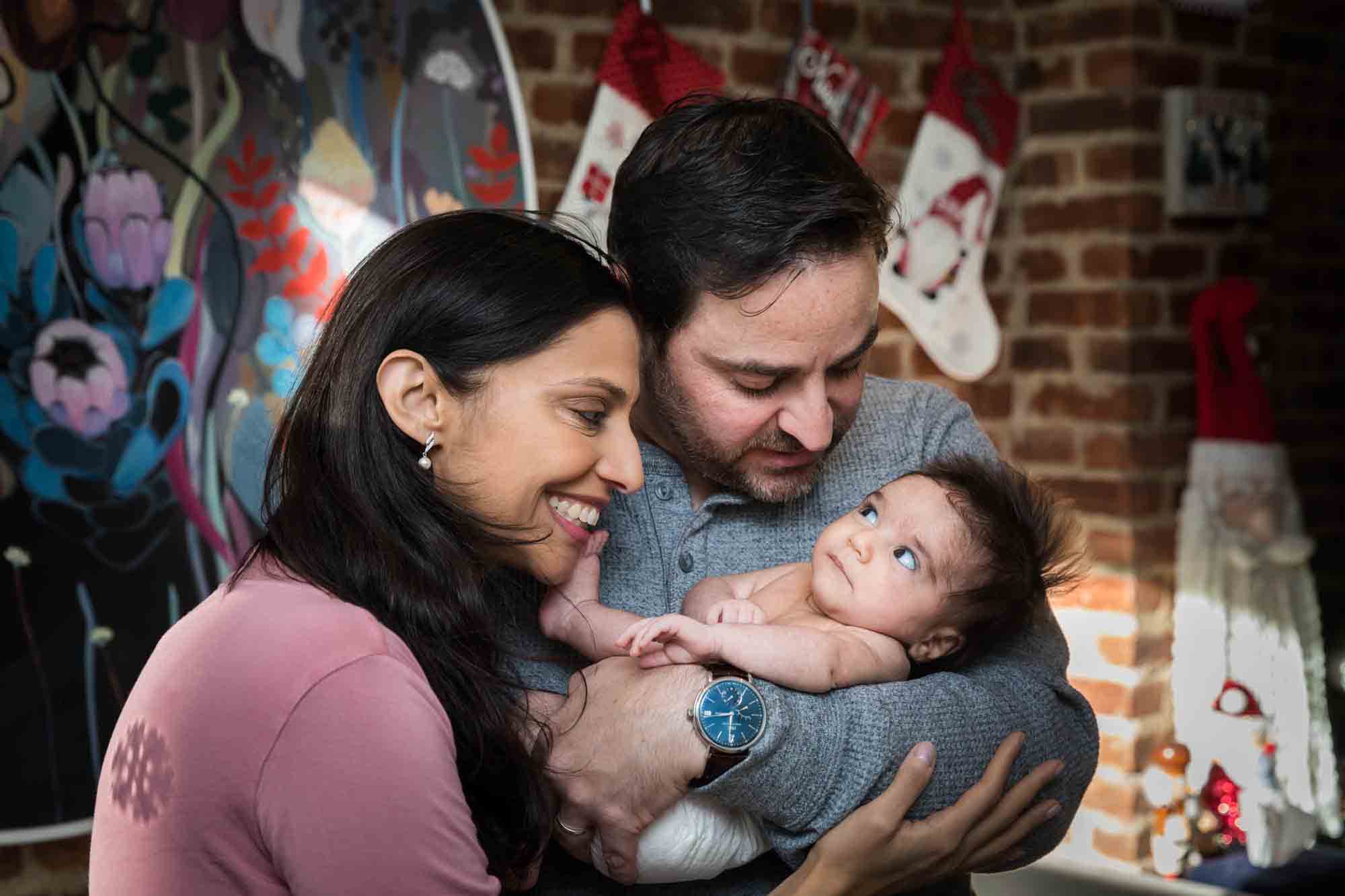 Parents holding newborn baby in front of brick wall