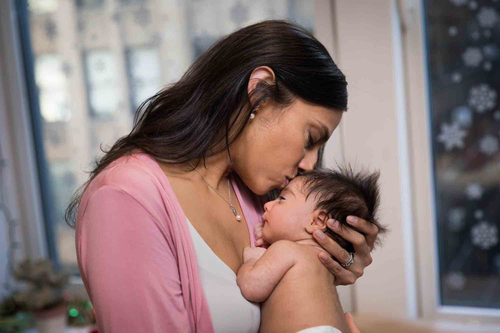 Mother kissing newborn baby on forehead while wearing pink shirt