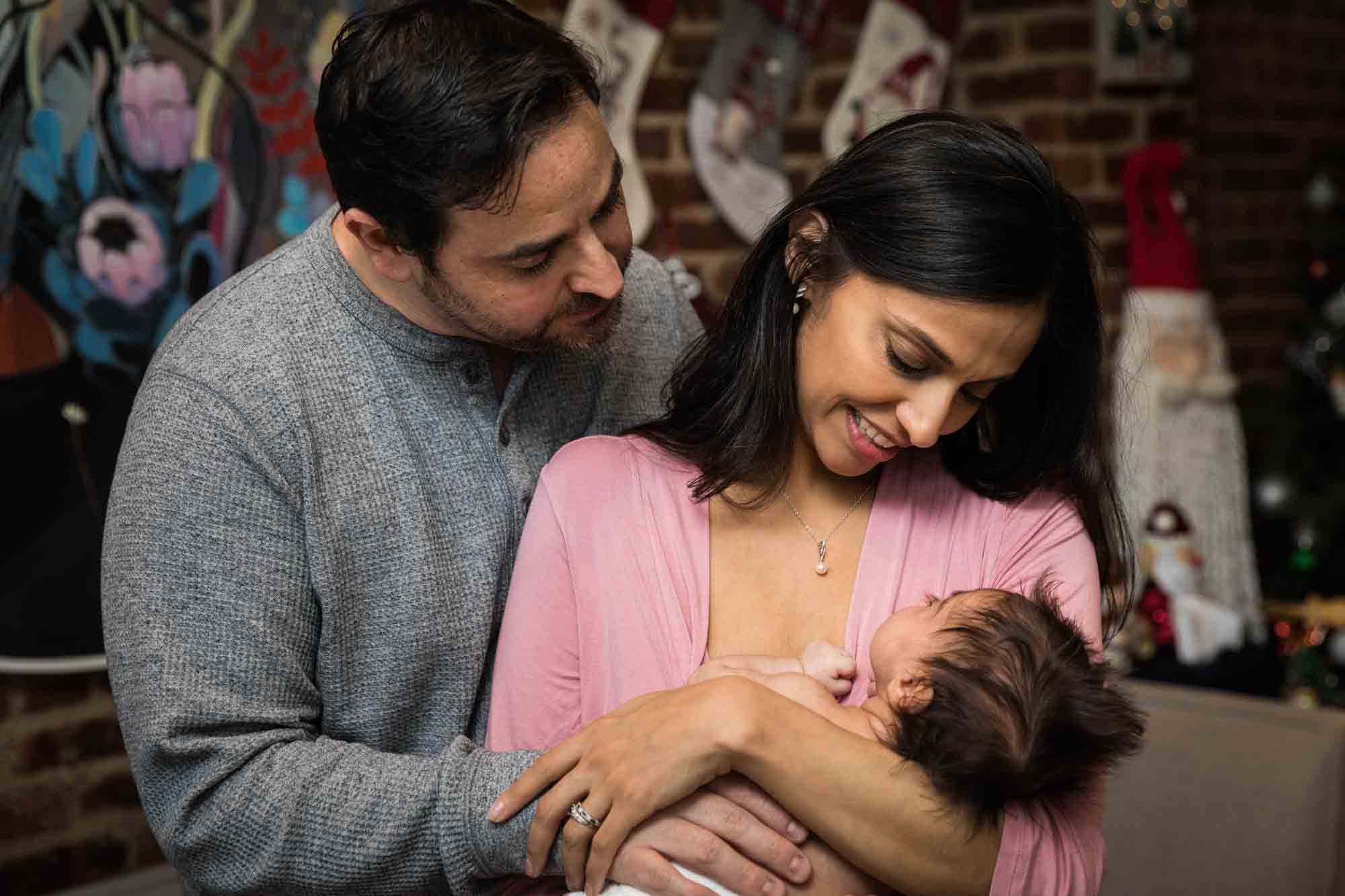 Parents holding newborn baby in front of brick wall