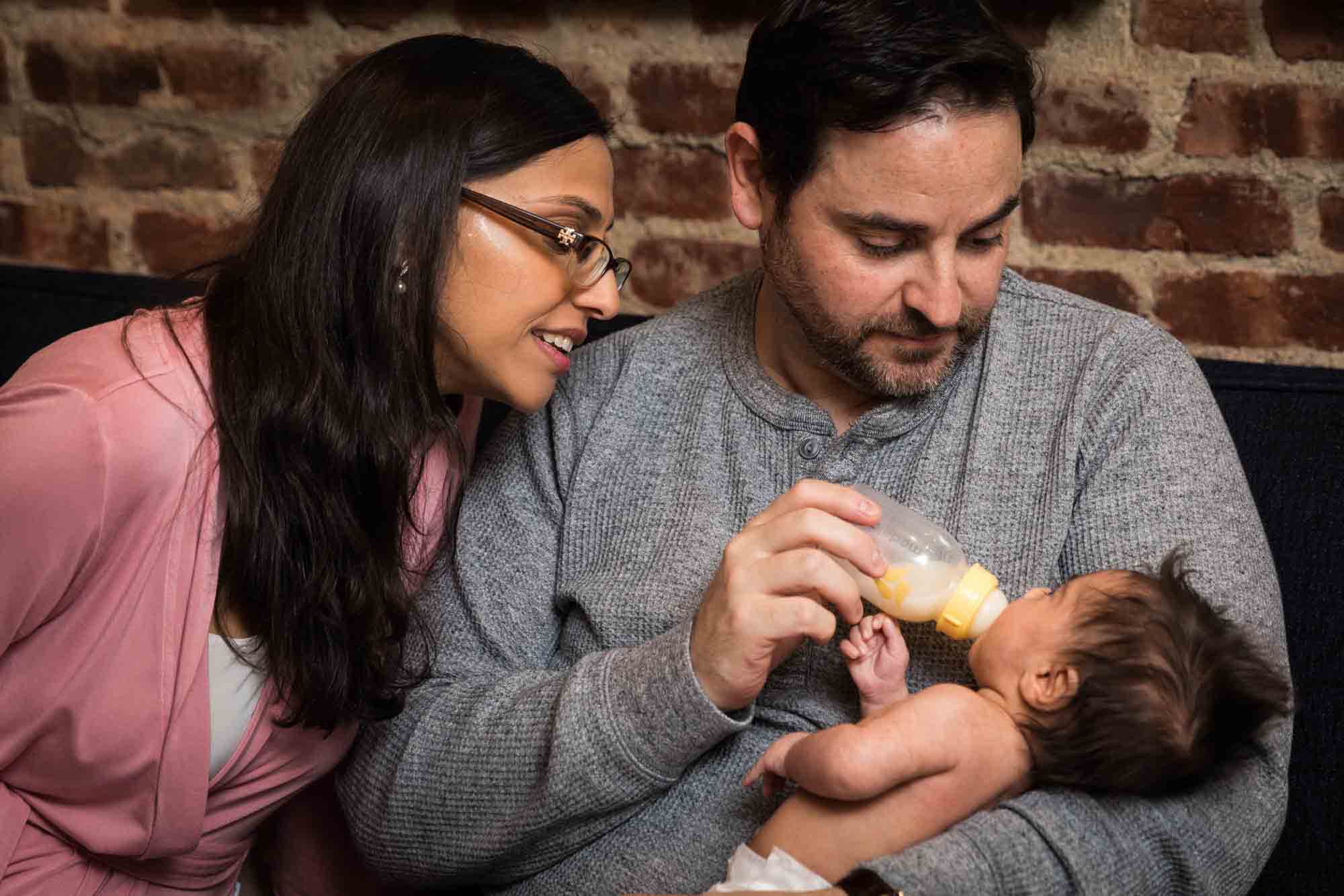 Parents feeding a bottle to a newborn baby during a Christmas-themed newborn photo shoot in NYC
