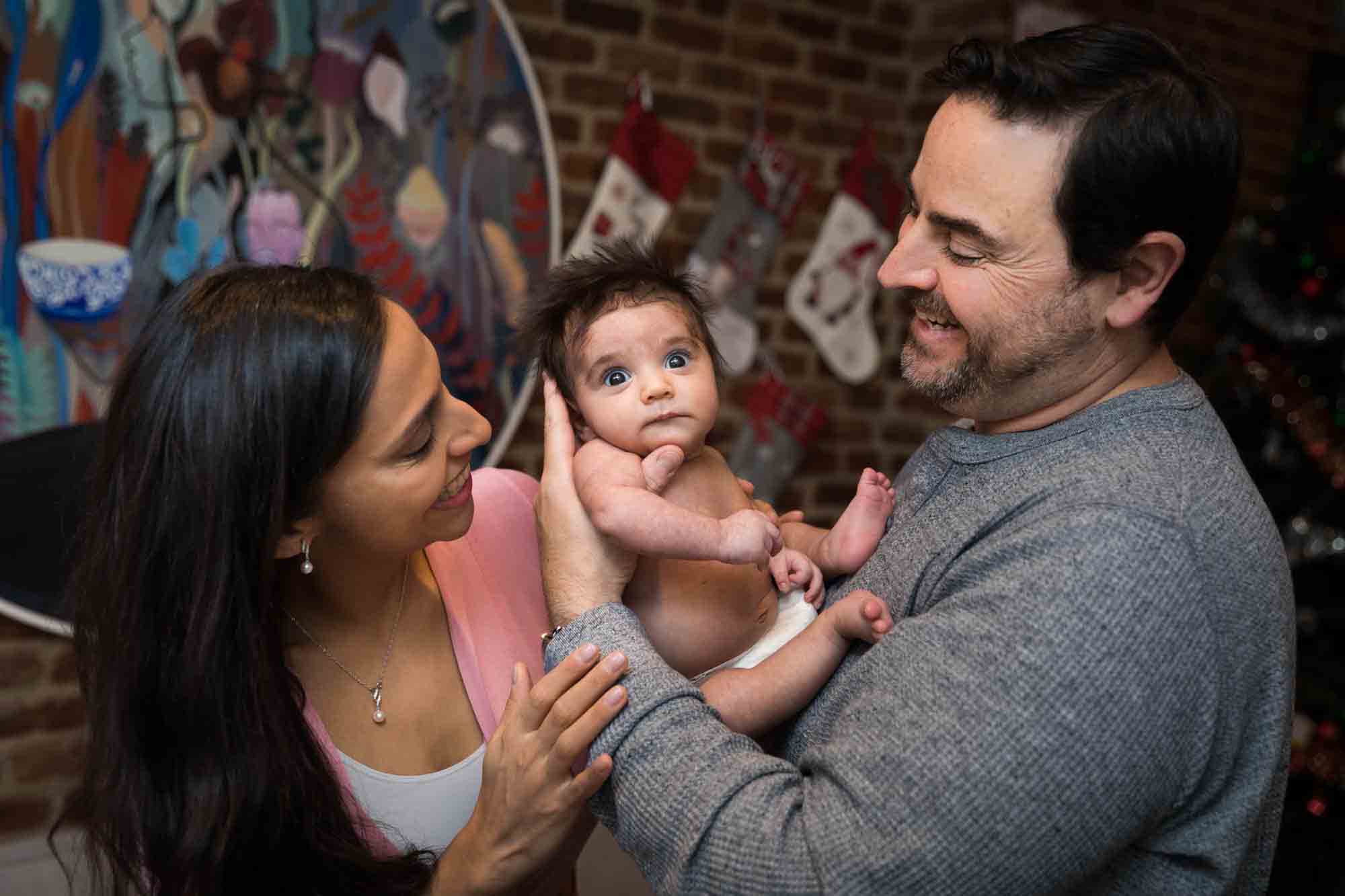 Parents holding newborn baby in front of brick wall during a Christmas-themed newborn photo shoot in NYC