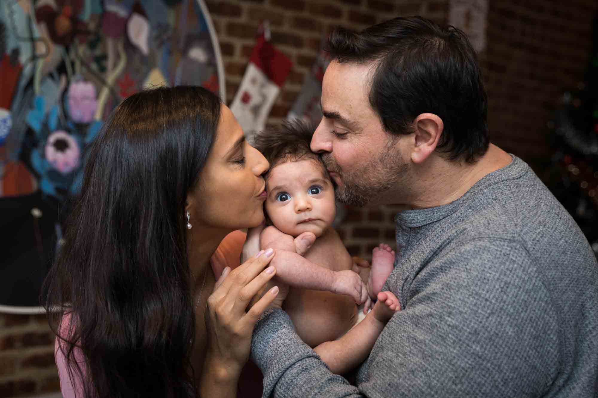 Parents kissing newborn girl on the cheeks during a Christmas-themed newborn photo shoot in NYC