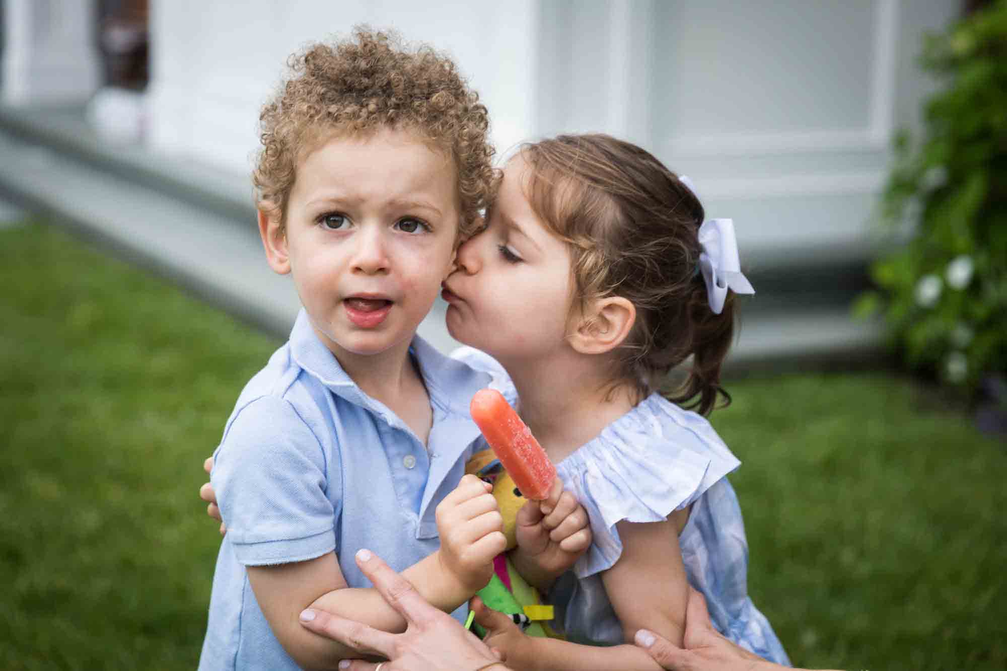 Little girl kissing side of brother's face for an article advertising family portrait gift certificates