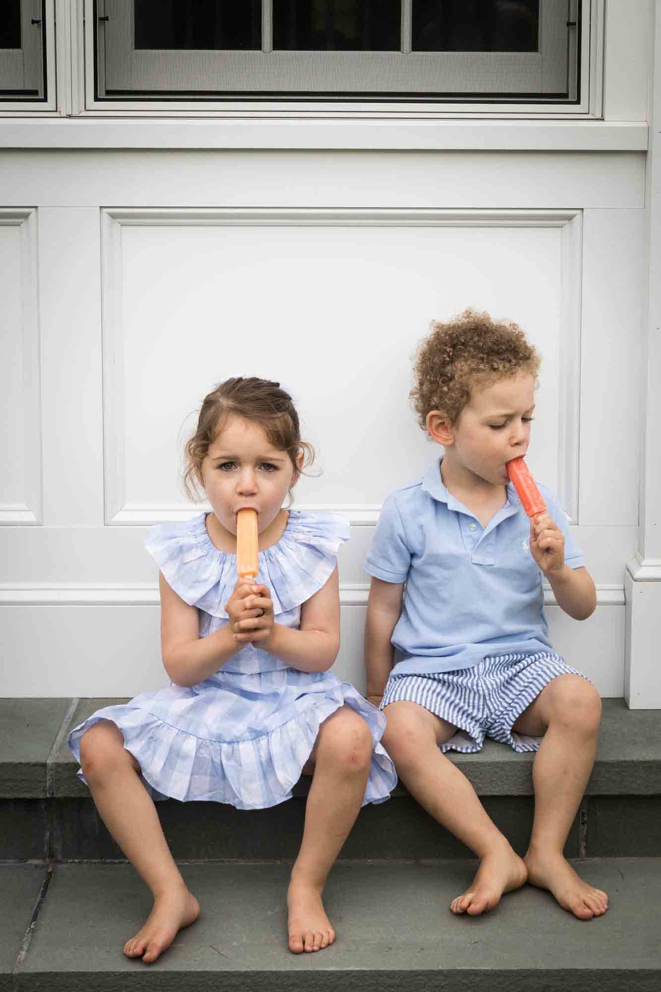 Little boy and girl sitting on steps eating popsicles